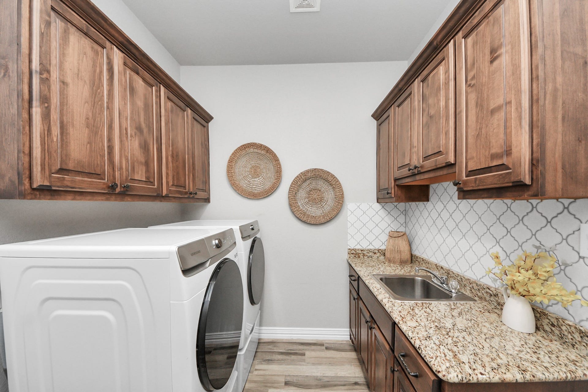 143 Pronghorn Place, Montgomery, TX 77316 Charming laundry room featuring elegant wood cabinetry, granite countertops, and modern appliances, complemented by stylish backsplash and decorative accents.