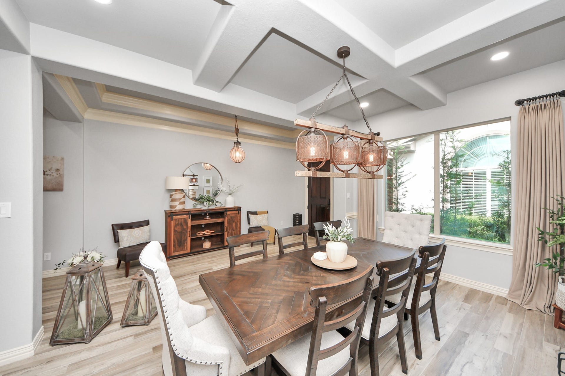 143 Pronghorn Place, Montgomery, TX 77316 A beautifully designed dining area features a coffered ceiling and elegant light fixtures, with large windows that invite natural light. The space includes a stylish wooden table, comfortable seating, and tasteful decor, creating a warm and inviting atmosphere.