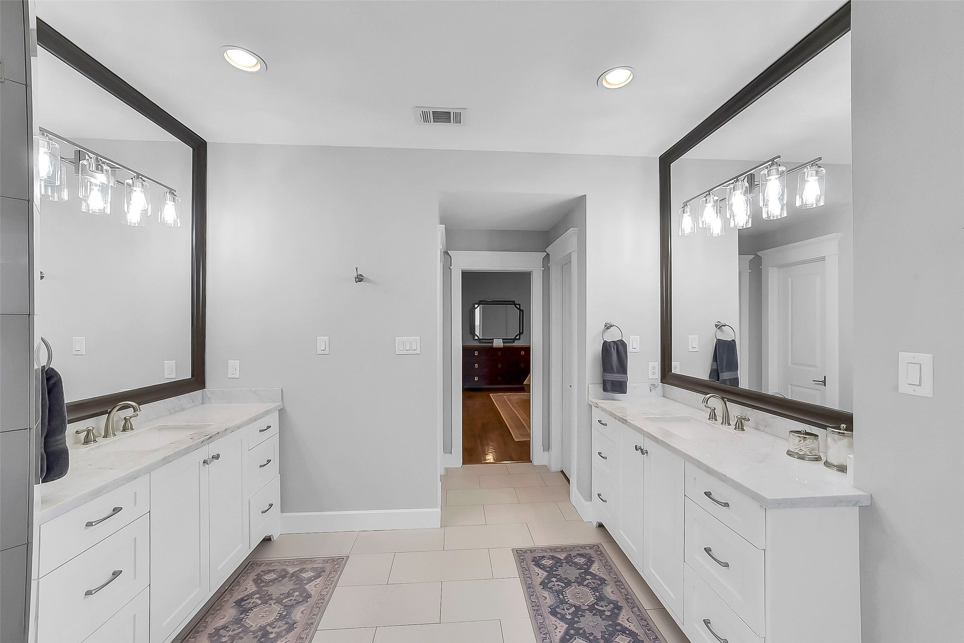 Another view of the primary bath featuring dual vanities with marble countertops, polished nickel fixtures, built-in vanity mirrors, and abundant cabinetry storage. Not shown is a large walk-in closet includes custom shelving, built-in drawers, and generous hanging space.
