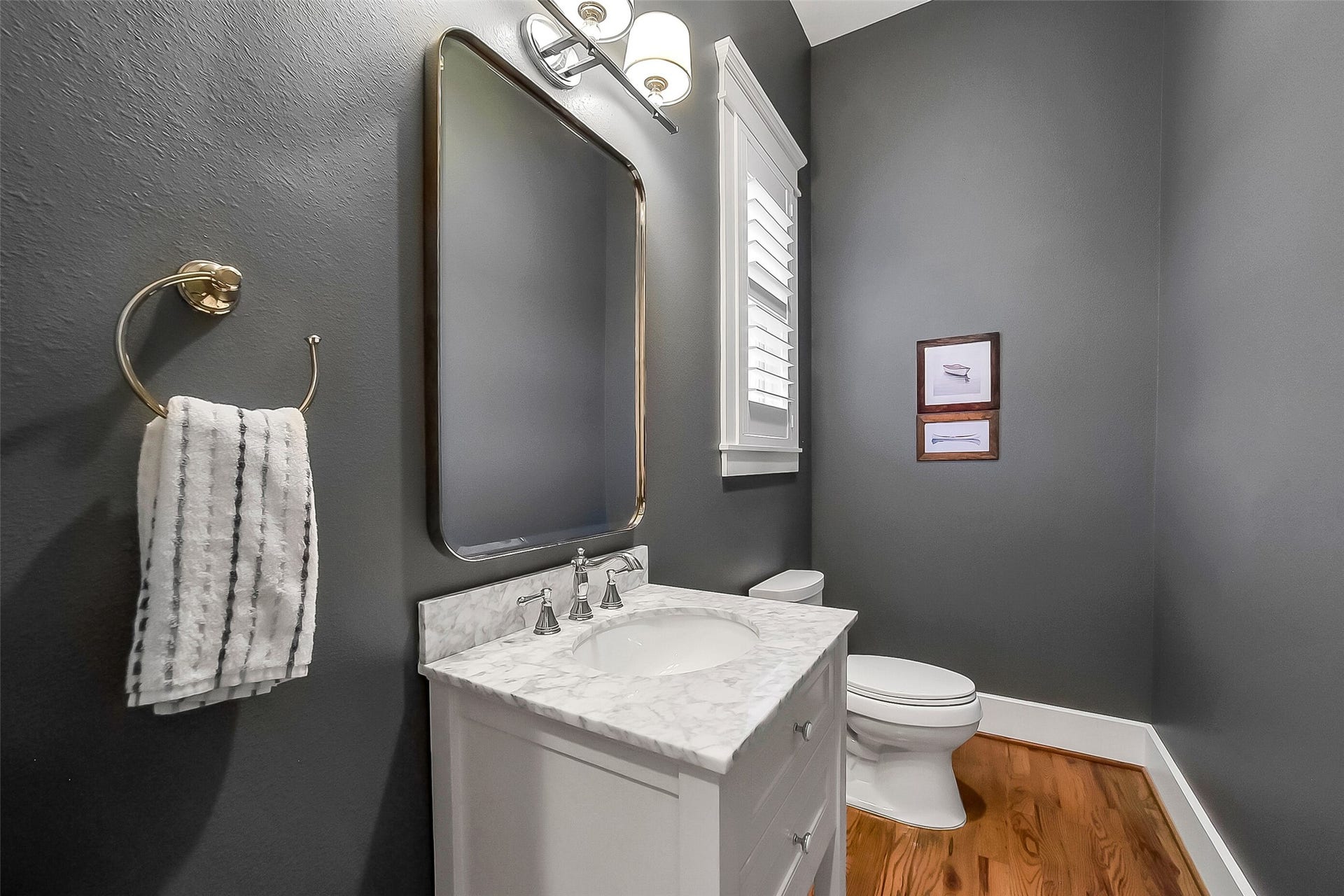 Conveniently located first-floor powder bathroom featuring a marble countertop vanity with undermount sink, polished nickel fixture, decorative lighting, plantation shutters, and hardwood flooring. Located adjacent to a large under-stair storage closet for additional functionality.
