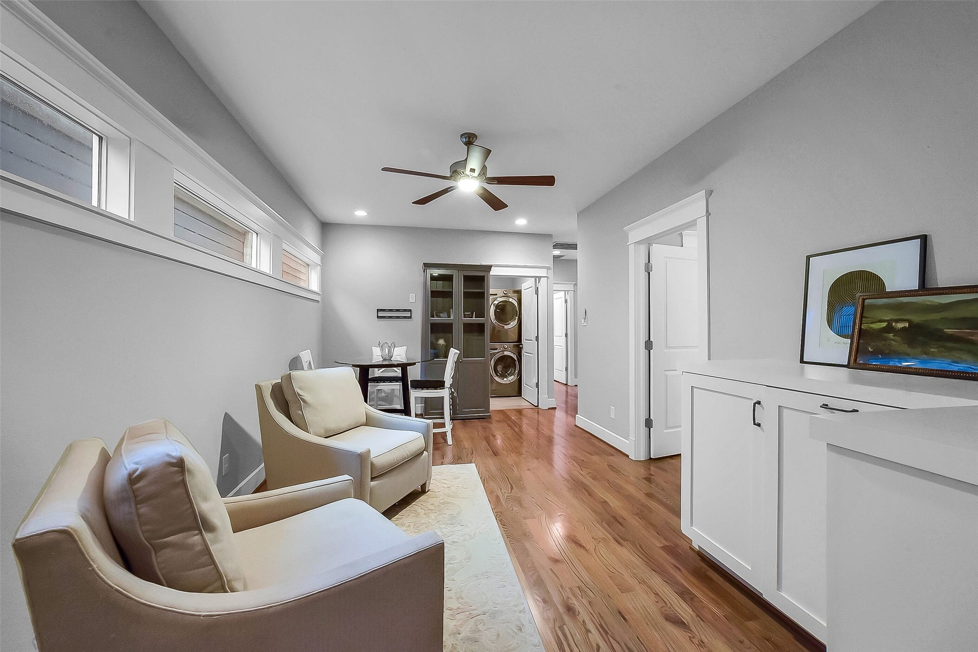 Another view of the flex space highlighting the abundance of natural light provided by three large windows. Hardwood floors, recessed lighting, and convenient access to the utility room and secondary bedrooms. Utility room straight ahead features a countertop with storage and a dry bar.