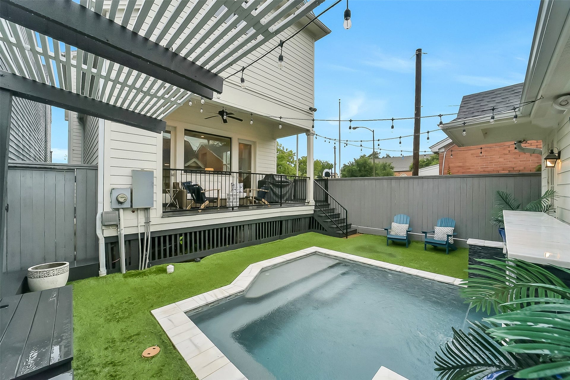 Another view of the backyard highlighting the pool, string lighting, detached 2 car garage to the right, and multiple spaces for gathering and entertaining. A wonderful extension of the home's living space.