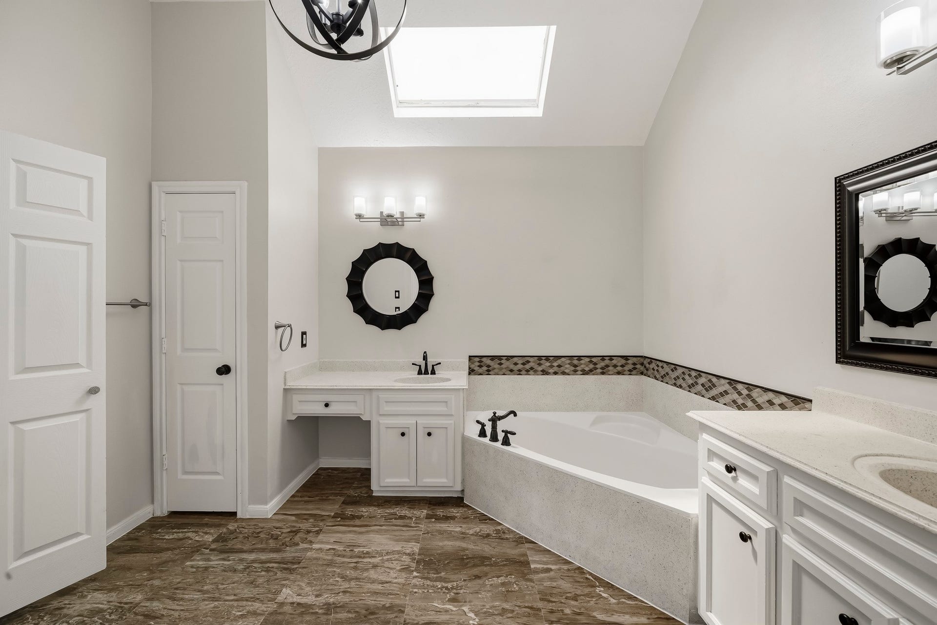 2611 Oxhill Court, Pearland, TX 77584 This spacious primary bathroom features a large soaking tub with decorative tile accents, dual vanity areas, and abundant cabinetry for storage. A large skylight fills the room with natural light and emphasizes the high ceiling, while tile flooring and neutral finishes create a bright, open atmosphere.
