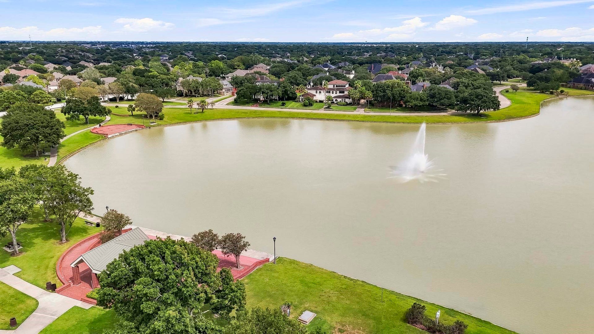 2611 Oxhill Court, Pearland, TX 77584 This beautiful aerial view showcases the communitys expansive lake surrounded by lush green space, mature trees, walking paths, and inviting recreational areas. The waterfront setting features open park space and gathering areas, creating a peaceful neighborhood amenity for enjoying the outdoors, scenic views, and community activities.