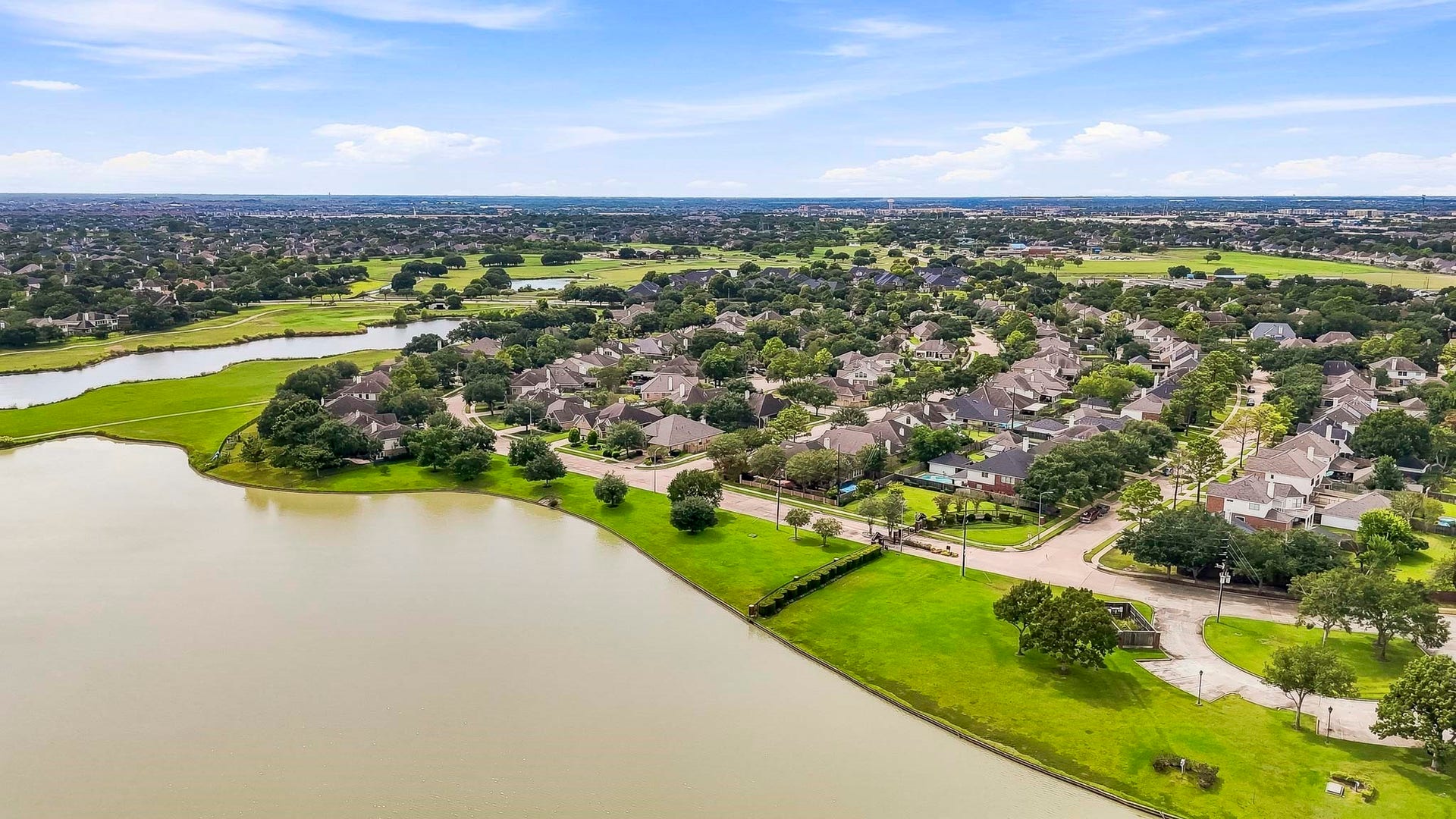 2611 Oxhill Court, Pearland, TX 77584 This beautiful aerial view showcases the communitys expansive lake surrounded by lush green space, mature trees, walking paths, and inviting recreational areas. The waterfront setting features open park space and gathering areas, creating a peaceful neighborhood amenity for enjoying the outdoors, scenic views, and community activities.