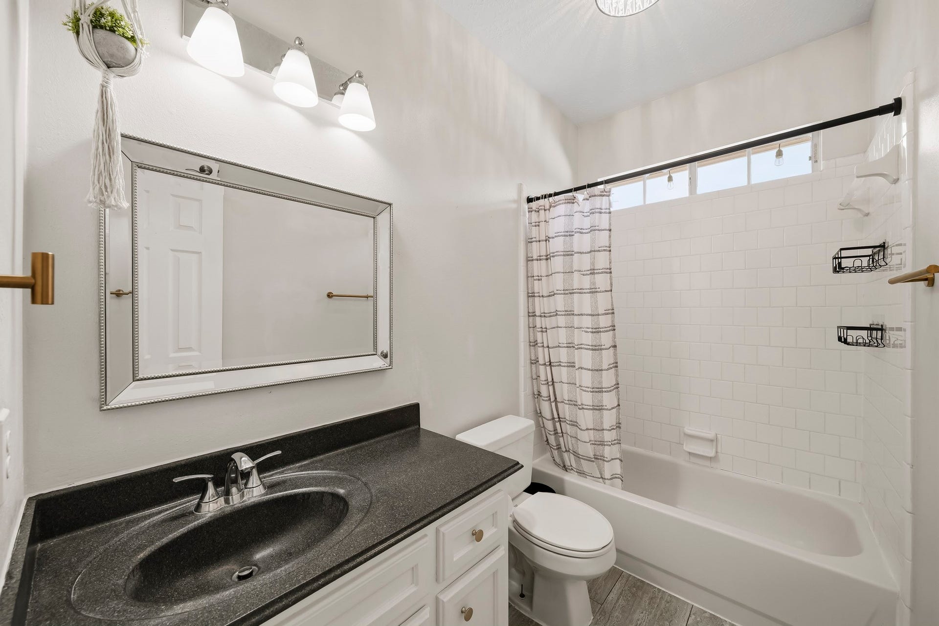 2611 Oxhill Court, Pearland, TX 77584 This bright full bathroom features a spacious vanity with white cabinetry, a dark countertop, and a large framed mirror. The tub-and-shower combination is surrounded by classic white tile and includes a high transom window that brings in natural light while maintaining privacy. Neutral finishes and updated fixtures create a clean, functional space.