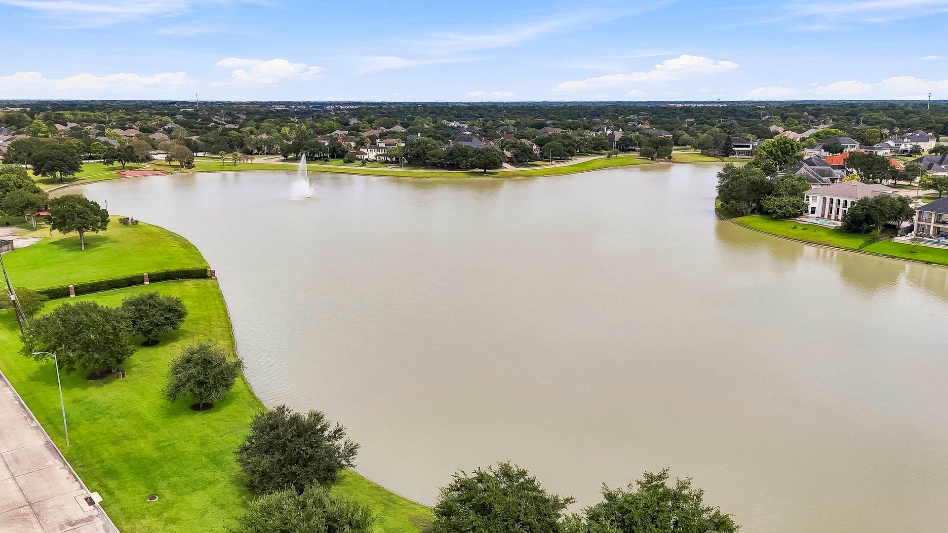 2611 Oxhill Court, Pearland, TX 77584 This beautiful aerial view showcases the communitys expansive lake surrounded by lush green space, mature trees, walking paths, and inviting recreational areas. The waterfront setting features open park space and gathering areas, creating a peaceful neighborhood amenity for enjoying the outdoors, scenic views, and community activities.