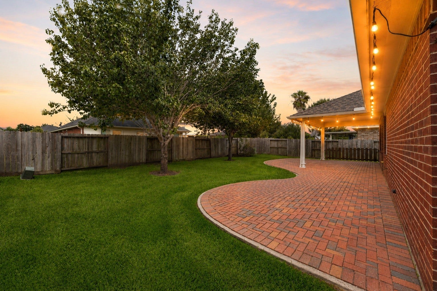 2006 Peonies Court, Pearland, TX 77581 As dusk settles, warm soffit lighting highlights the rear brick elevation and surrounding greenery, lending the backyard a welcoming glow as the day winds down.