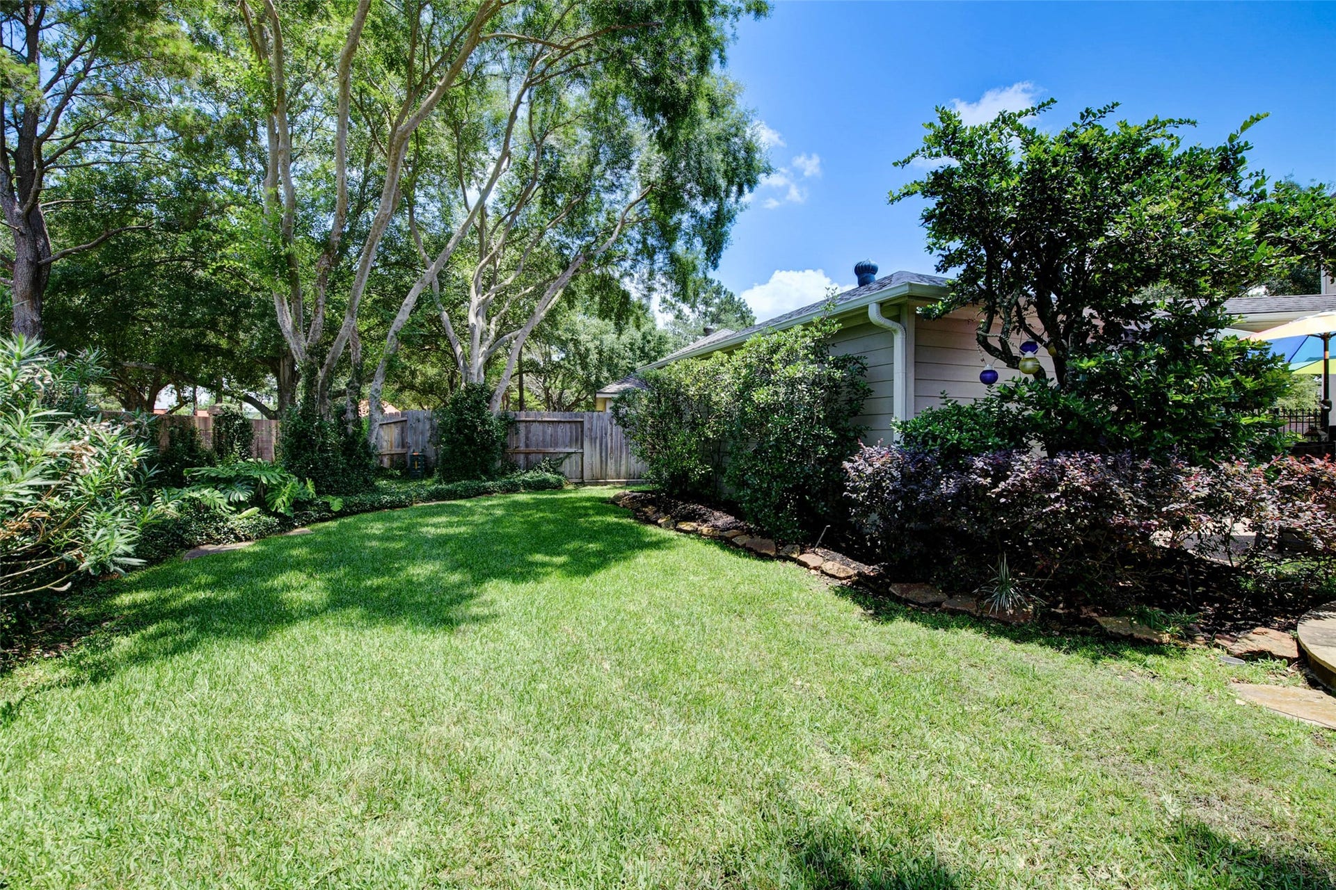 This photo showcases a lush, well-maintained backyard with a spacious lawn, mature trees, and attractive landscaping. The area is private and fenced, providing a peaceful outdoor space for relaxation or entertainment.