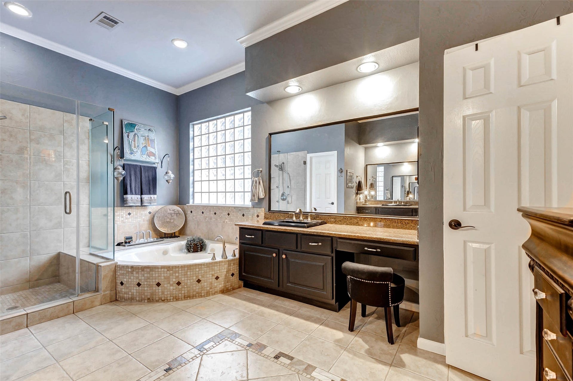 This spacious bathroom features a modern design with a large glass-enclosed shower, a luxurious corner jetted bathtub, and a dual-sink vanity with granite countertops. The space is enhanced by recessed lighting and stylish tile flooring. Shower has seating. The shower fixture has hand held and 4 body sprays and tub also has a hand held sprayer.