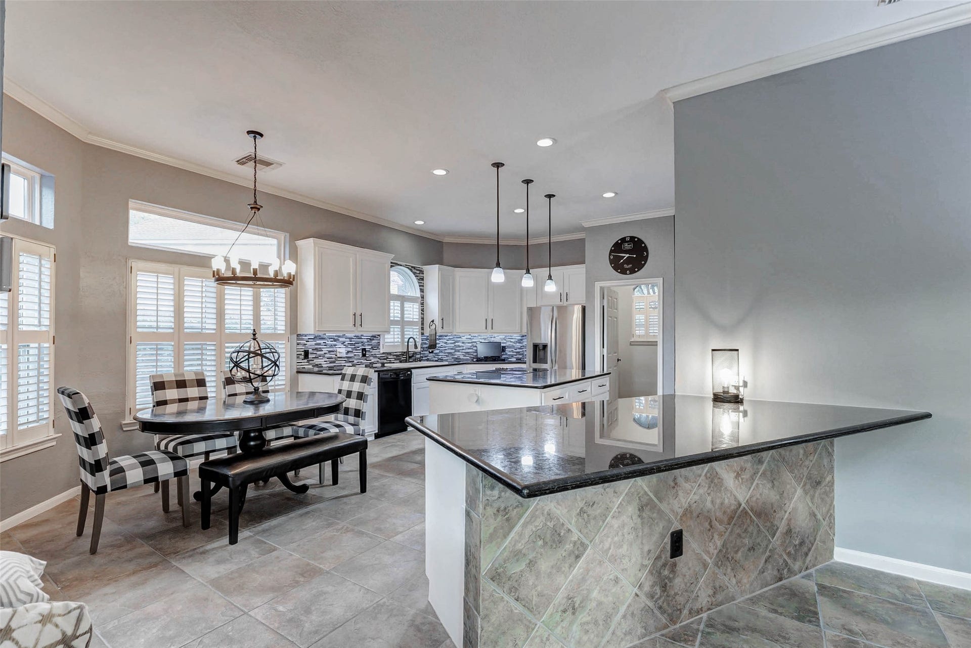 This modern kitchen features sleek white cabinetry, a stylish tile backsplash, and stainless steel appliances. It includes spacious island and large peninsula with breakfast bar. Both counter height, one with pendant lighting, adjacent to a cozy breakfast room, creating a bright and inviting space.