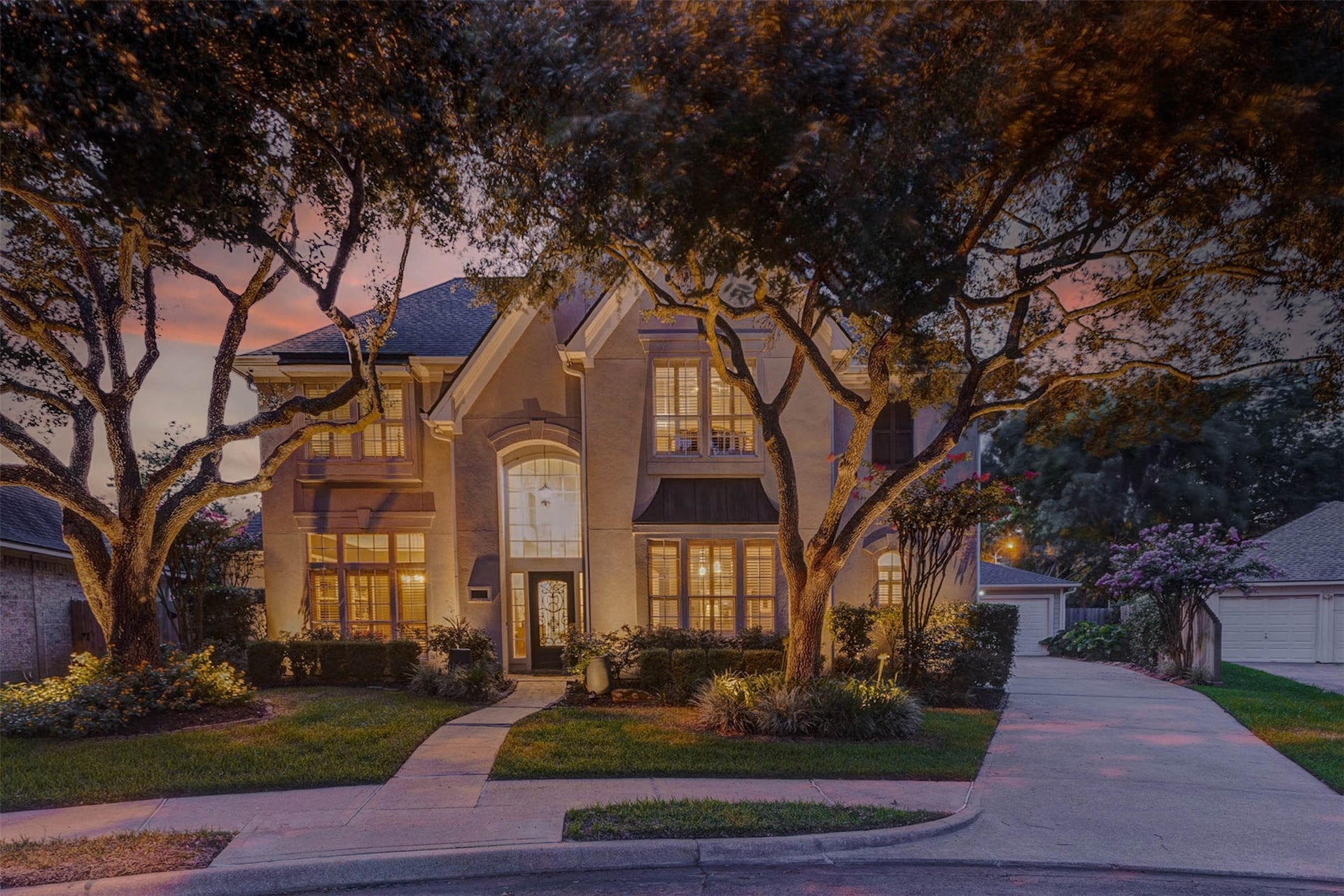 This stunning two-story home features elegant architectural details with large windows and a welcoming entrance. Surrounded by mature trees and well-maintained landscaping, it offers a charming curb appeal. The driveway leads to a spacious garage, perfect for family living.