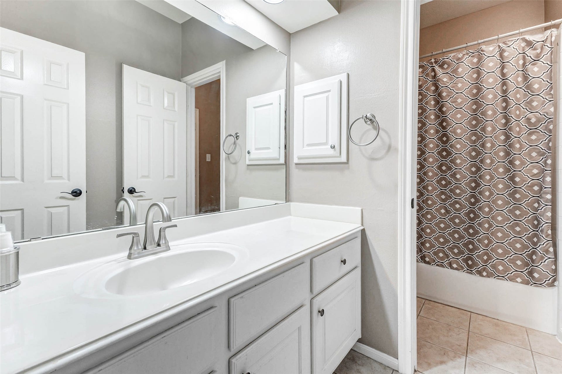 This Jack & Jill bathroom features a clean, modern design with a large vanity and ample storage. It includes a single sink, a mirrored cabinet, linen closet and a shared toilet-shower-tub combo. The neutral tones and tiled flooring create a fresh and inviting atmosphere.