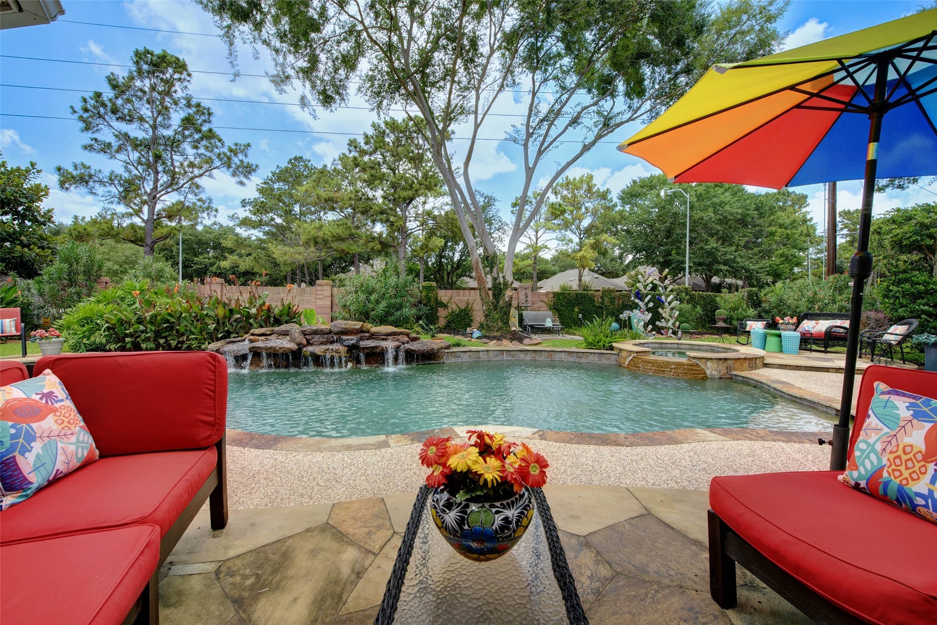 This backyard features a serene pool with a waterfall, surrounded by lush greenery. It includes a cozy seating area, perfect for relaxation and entertaining.