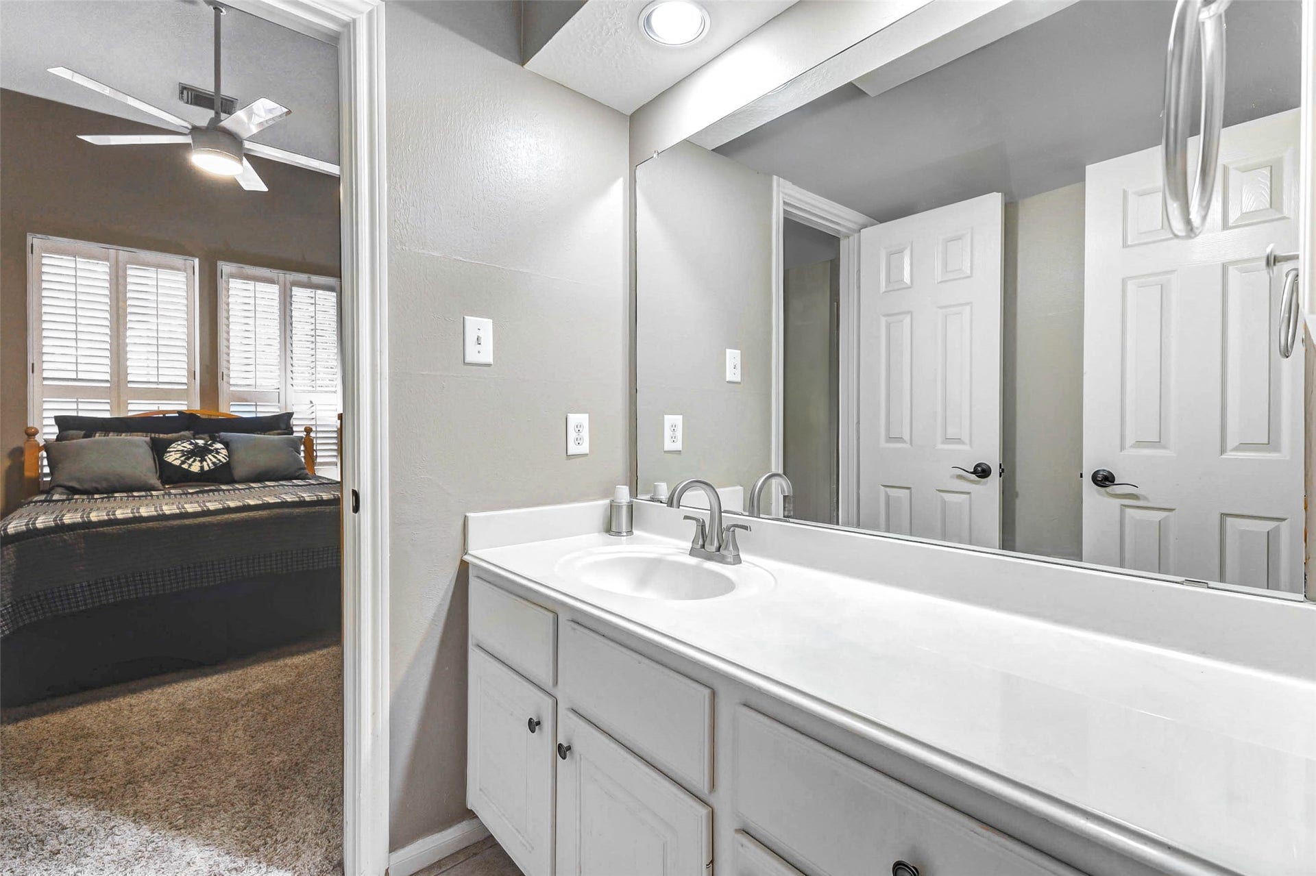 This photo shows the Jack & Jill bathroom with a sleek white vanity and large mirror, adjacent to a bedroom.  Features a large linen closet.