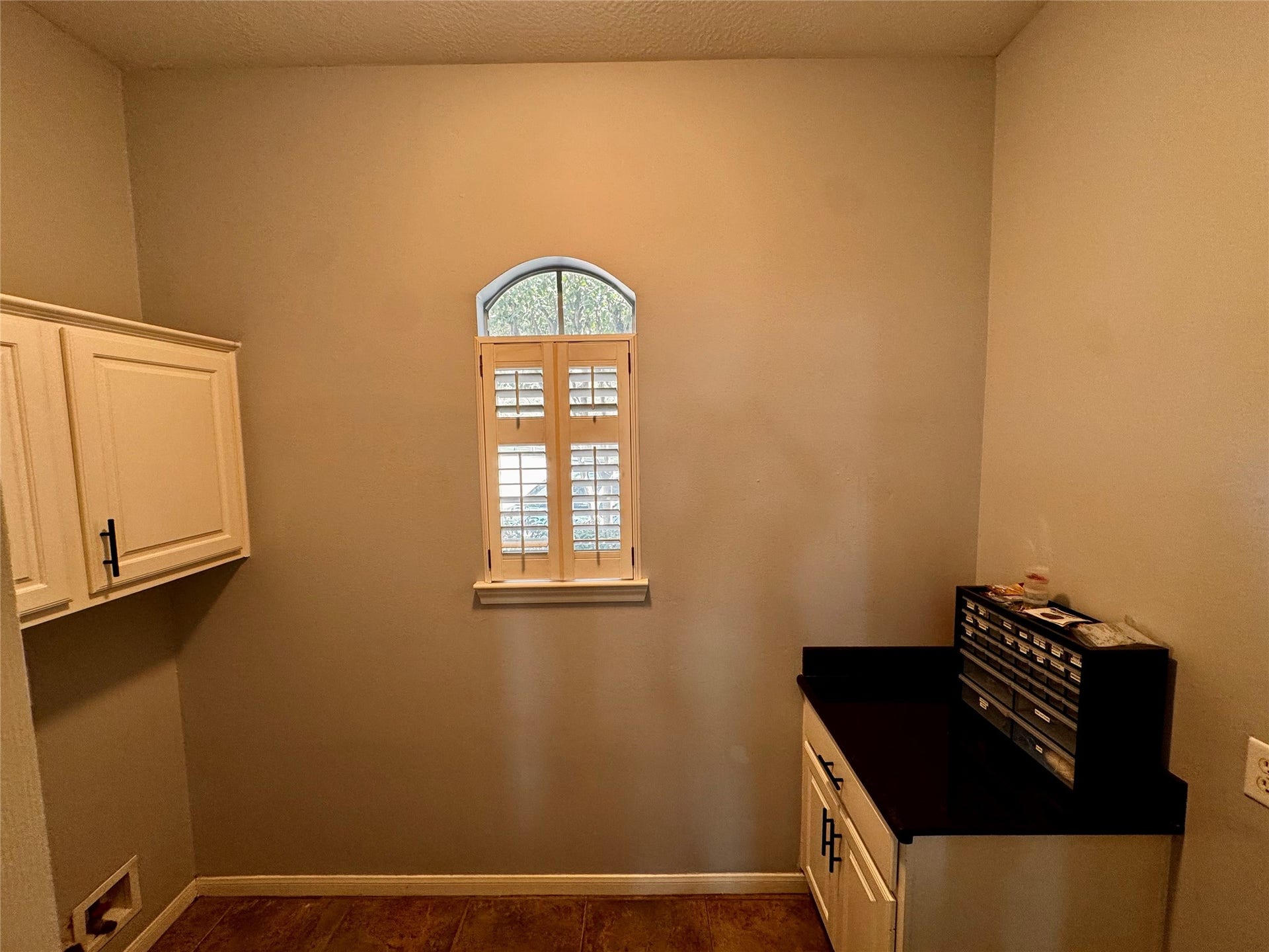 This laundry room features ample white cabinetry for storage, a sleek black granite countertop, and a window with shutters, creating a bright and functional space. Room for a full size refrigerator too!