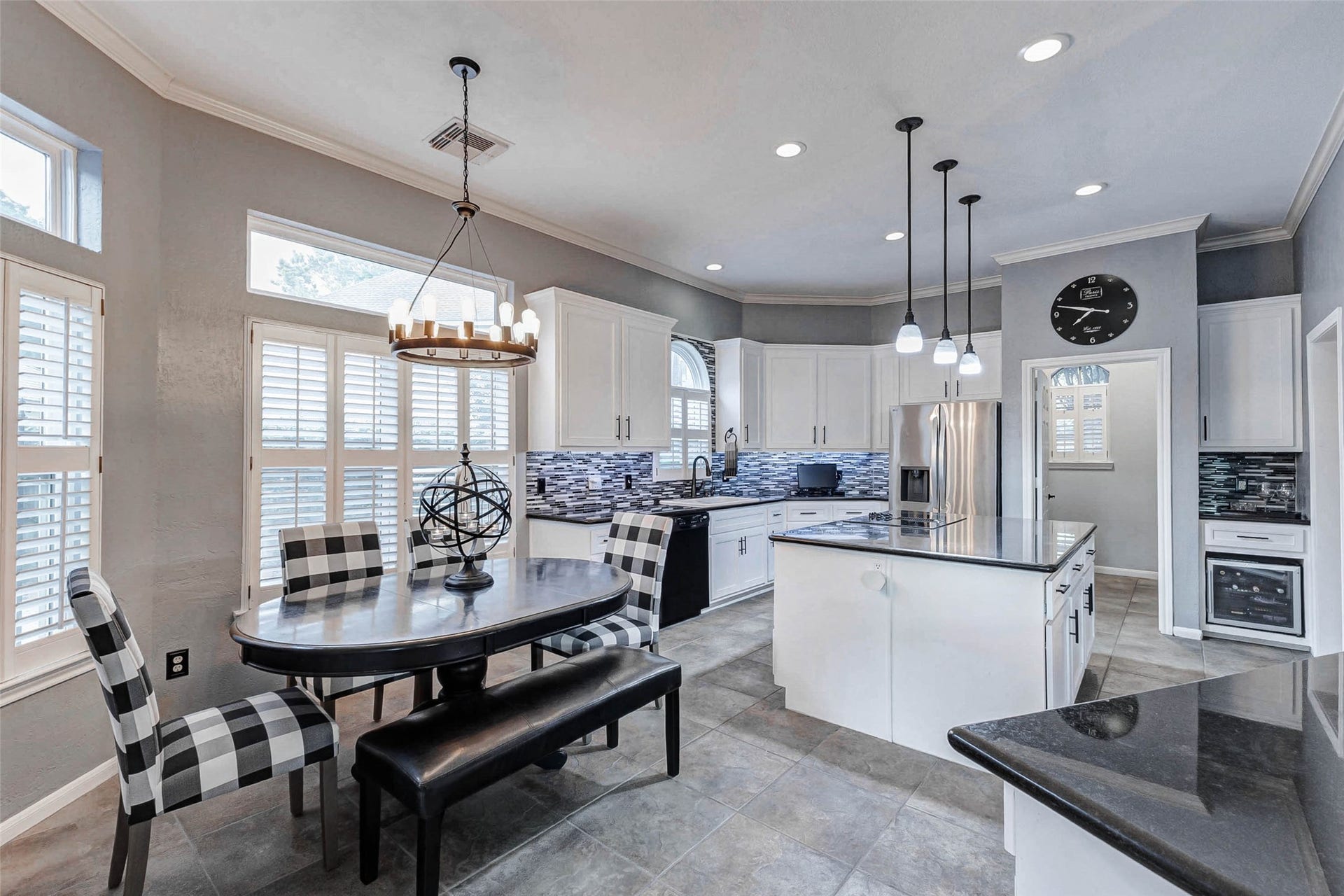 Bright and modern kitchen with ample natural light, featuring white cabinetry, a large island with pendant lighting, and black appliances. The breakfast room has space for a large table. Note, the large island in this kitchen area, Plus a bonus peninsula with breakfast baris open to the family room. Note, the wine fridge at the Butler's Pantry will stay.