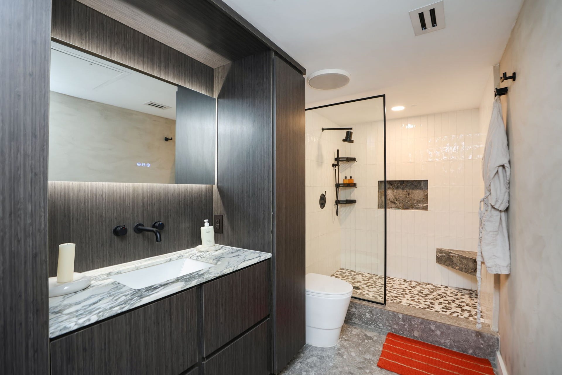 Luxury abounds in the primary bath featuring Calacutta Viola marble vanity top, dark wood-grain cabinetry, and a backlit LED-illuminated mirror.
