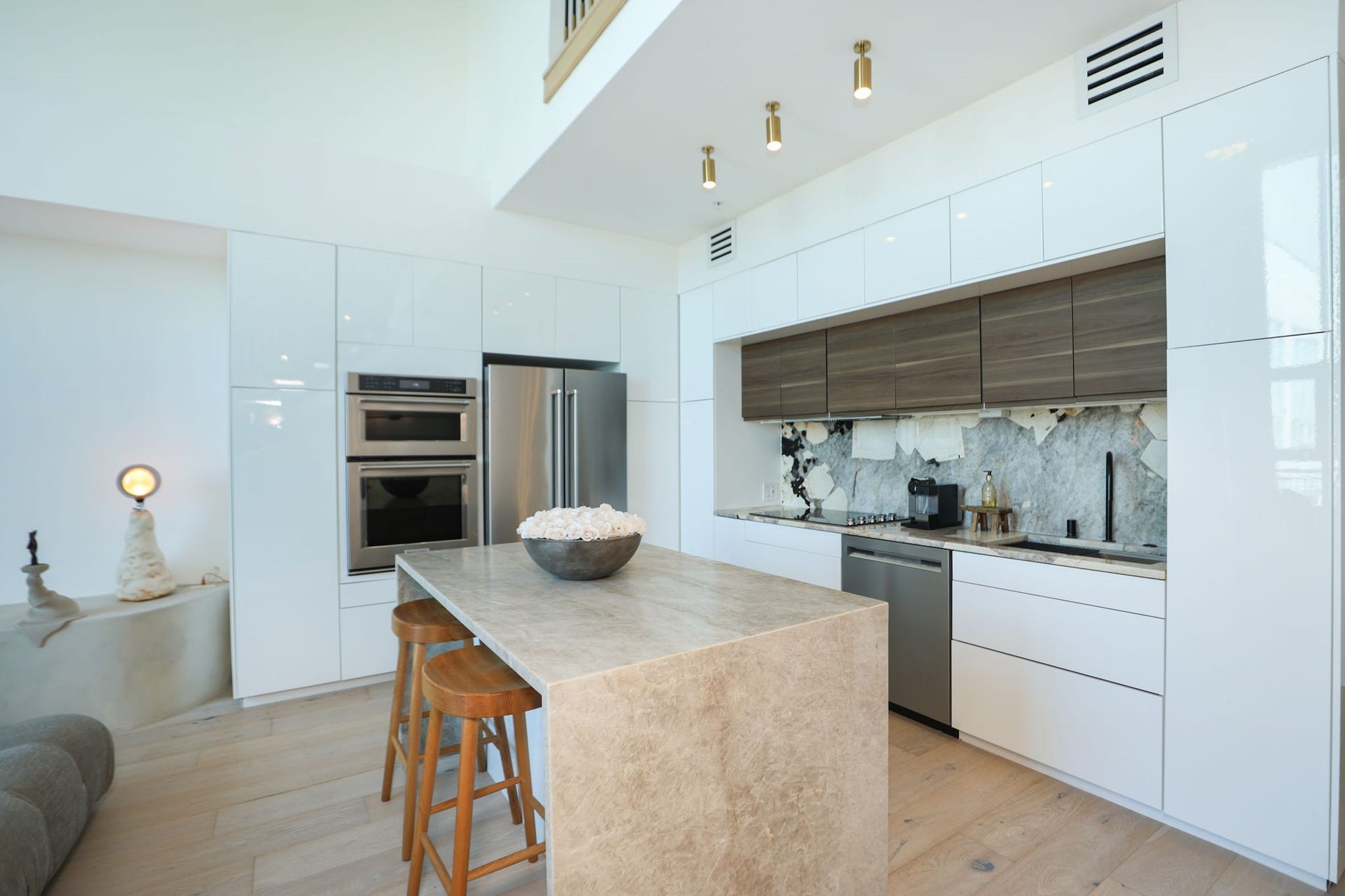 Calcutta Viola marble, waterfall island, sleek high-gloss white cabinetry with contrasting wood-grain accents, and integrated lighting define this gorgeous kitchen.