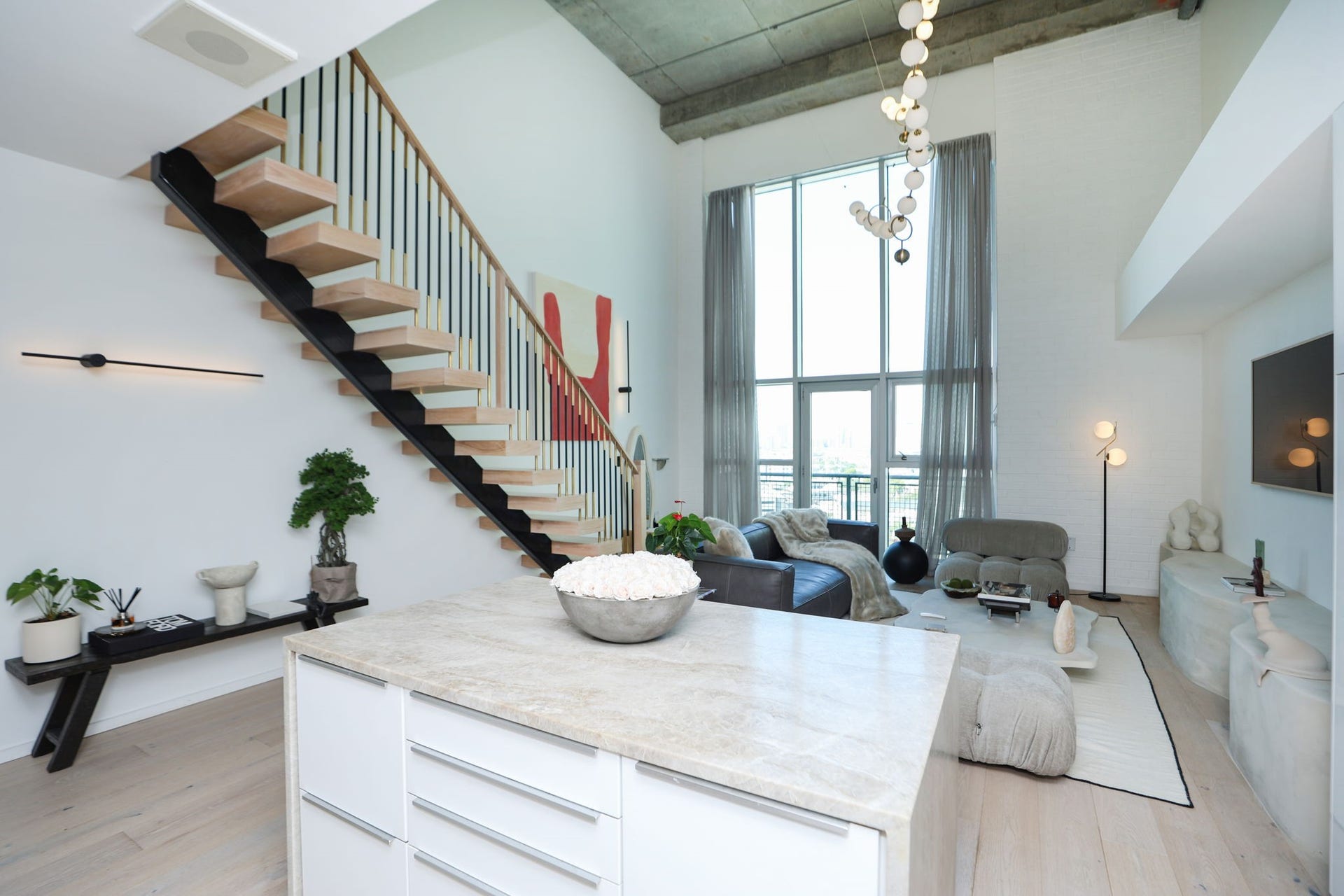 Taj Mahal quartzite waterfall island with built-in storage, open to the living are with double height windows. Smart window blinds adjust for privacy.