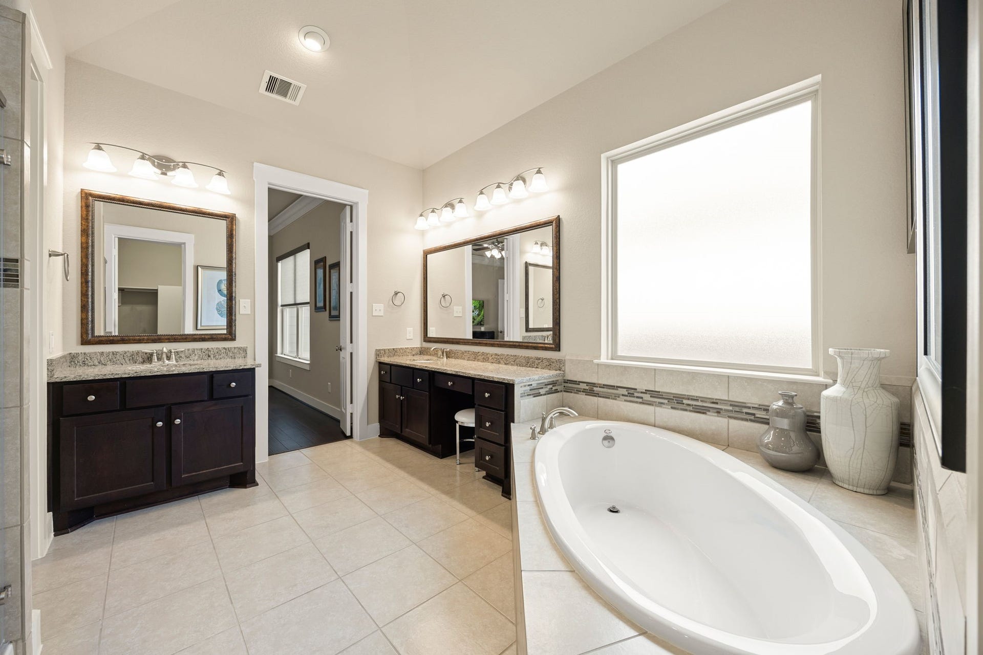 14 Kendrick Pines Boulevard, The Woodlands, TX 77389 Indulge in a spa-like experience within this luxurious primary bath, featuring dual vanities with rich dark cabinetry and elegant stone surfaces.