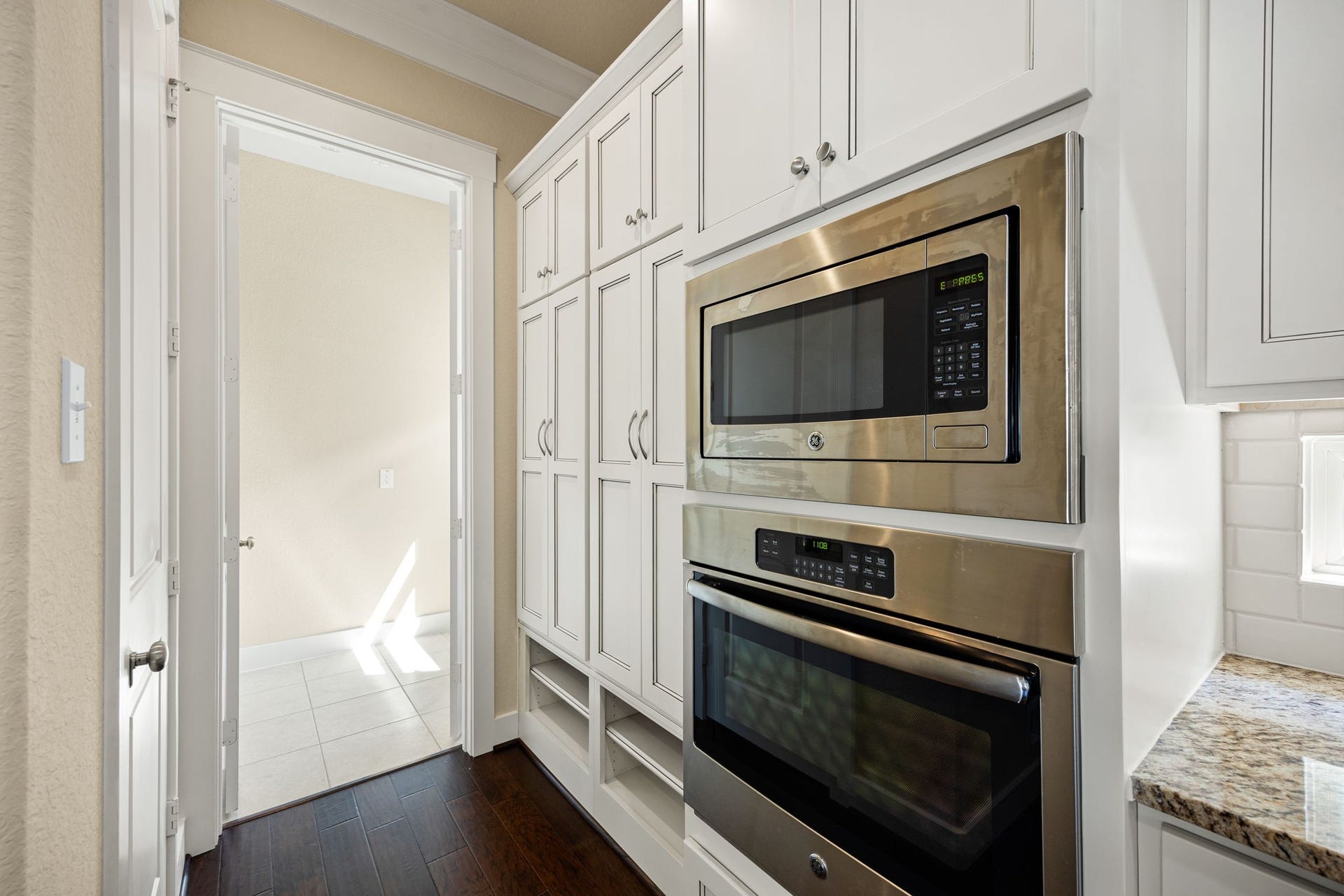 14 Kendrick Pines Boulevard, The Woodlands, TX 77389 This sleek culinary corner showcases premium stainless steel appliances, featuring a built-in wall oven and microwave integrated seamlessly into crisp white cabinetry. The floor-to-ceiling pantry provides abundant storage, while the rich hardwood floors offer a sophisticated contrast to the bright, modern finishes. This space is a testament to functional luxury, designed for the modern home chef.