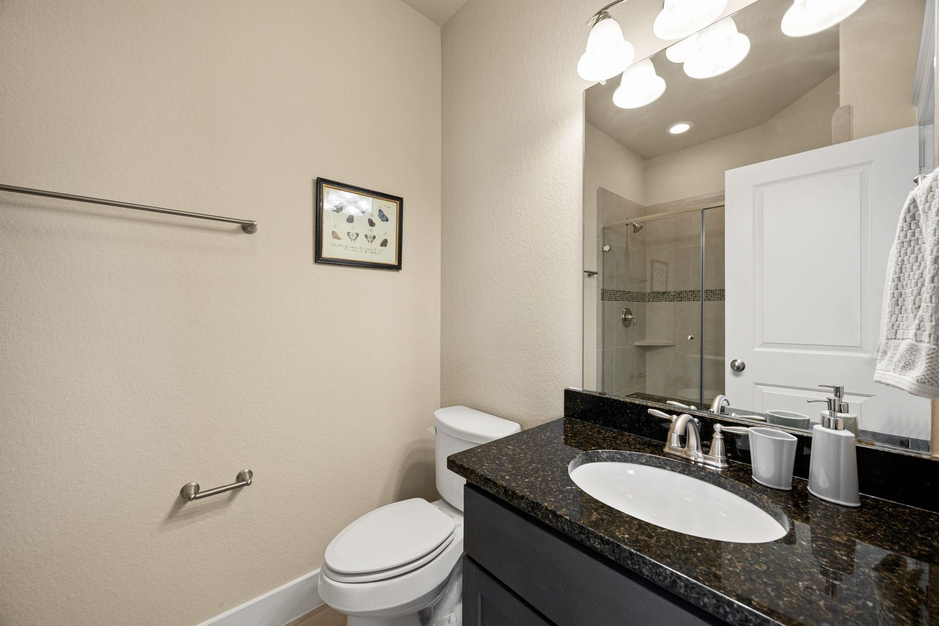 14 Kendrick Pines Boulevard, The Woodlands, TX 77389 This contemporary full bath serves as a stylish and functional space for family or guests. A sleek dark vanity is topped with a polished black granite counter, offering a sophisticated contrast to the bright, neutral walls. The space is anchored by a glass-enclosed walk-in shower featuring classic tile work, while the modern light fixture and crisp white trim enhance its clean, upscale feel.