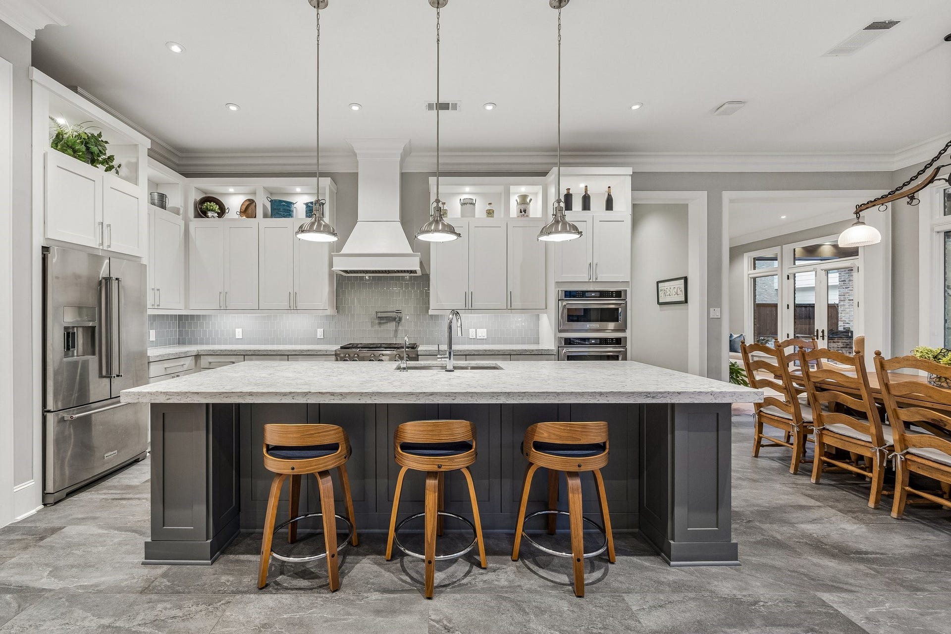 The generously proportioned island serves as the centerpiece of the kitchen, offering abundant preparation space, an undermount sink, and comfortable seating for casual dining.  White Shaker Style cabinetry with a contrasting Charcoal-Gray Island and three polished pendant lights.  Illuminated upper display cabinets, Crown Molding, LED recessed lighting, under cabinet lighting, pot filler and stainless appliances.
