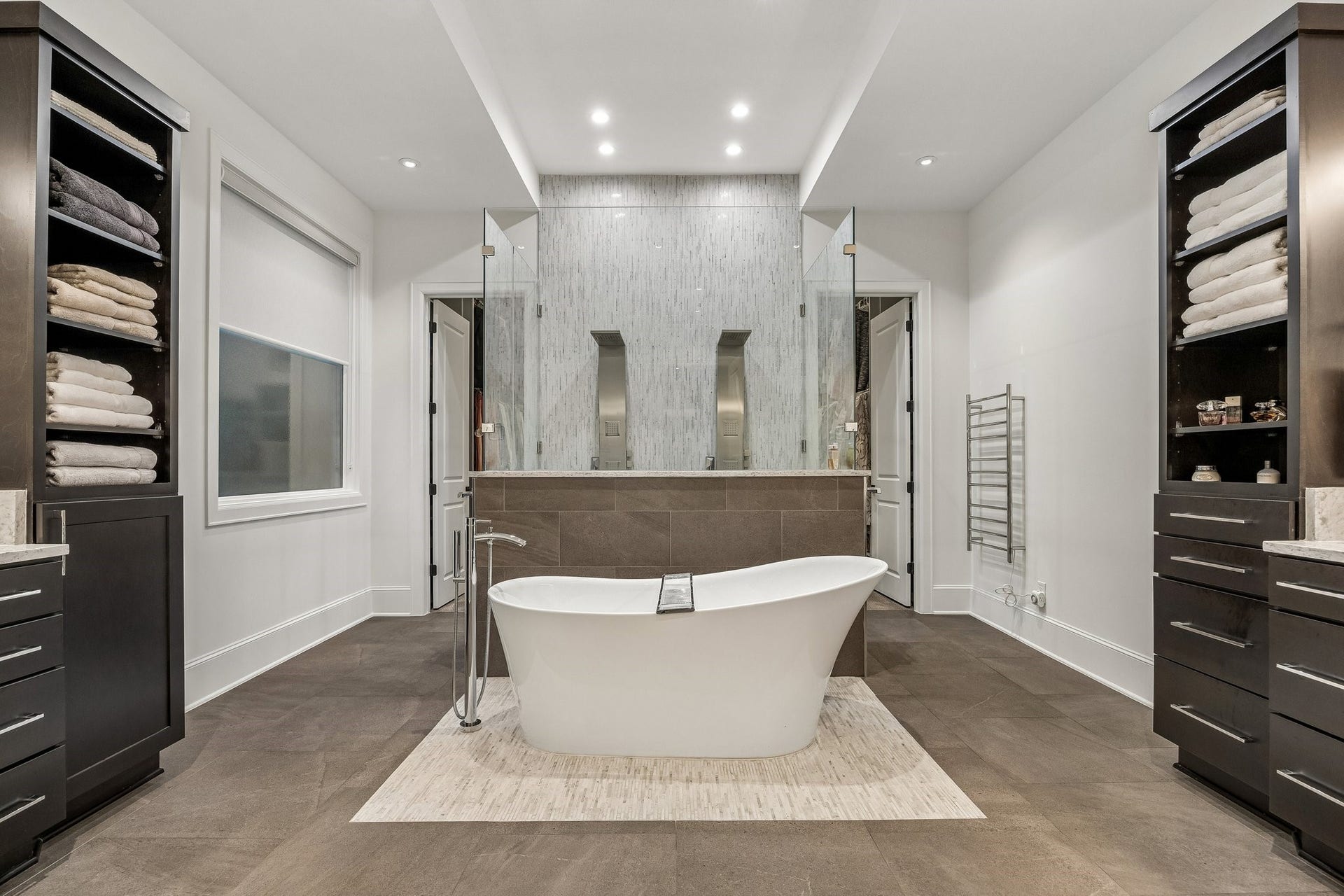 This extraordinary primary bathroom is a stunning expression of contemporary luxury, showcasing sophisticated architectural design, exquisite finishes, and a beautifully balanced, spa-inspired atmosphere. The expansive layout features a striking freestanding soaking tub positioned as the room's dramatic centerpiece, creating an inviting sanctuary for relaxation and rejuvenation.