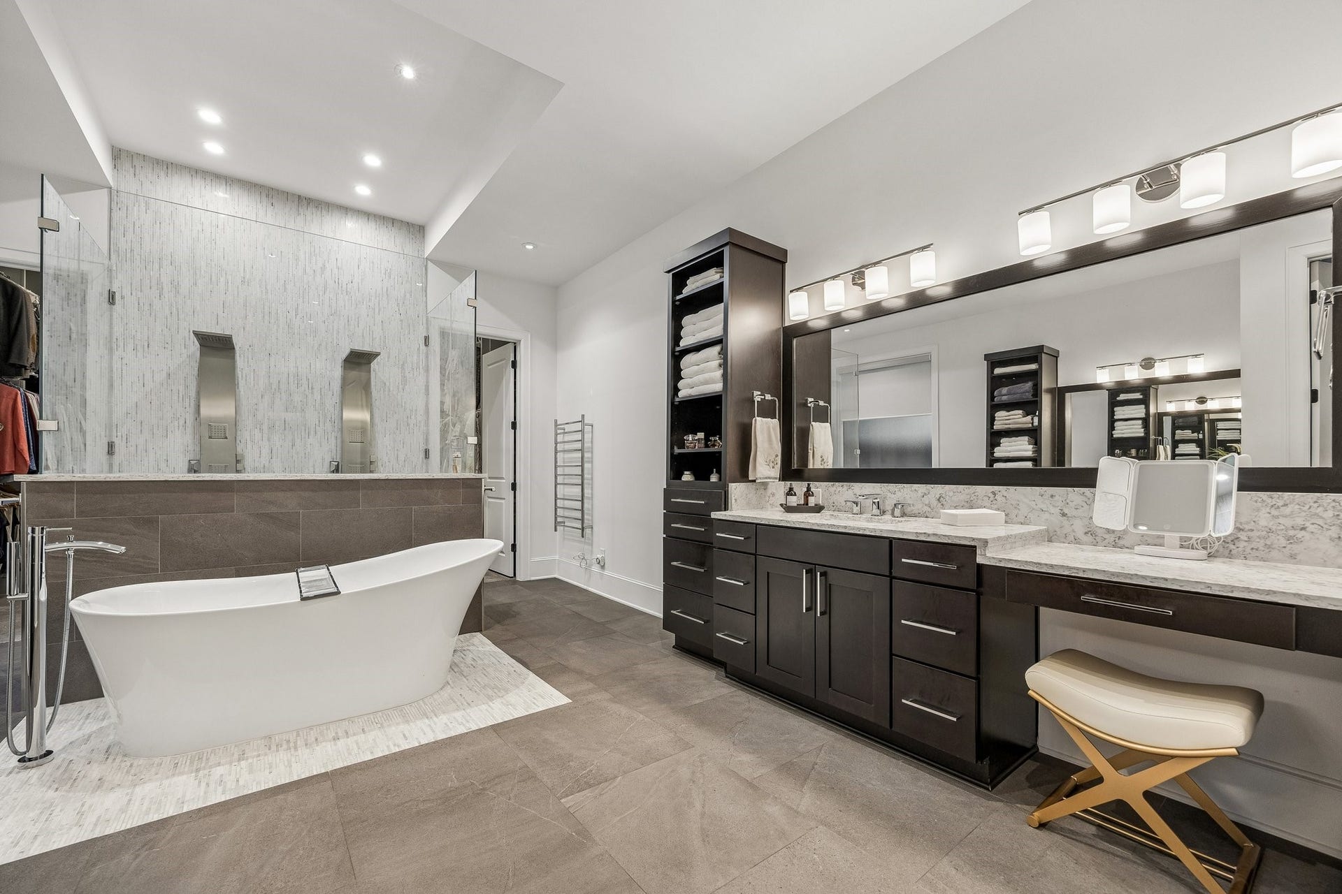 Rich charcoal-toned tile flooring provides a beautiful contrast to the Classic Carrara Stone Counters.  Shaker Style Cabinetry, vanity, pendent lighting, tons of linen storgae and open shelving.  There is also a towel warmer conveniently located outside the shower.