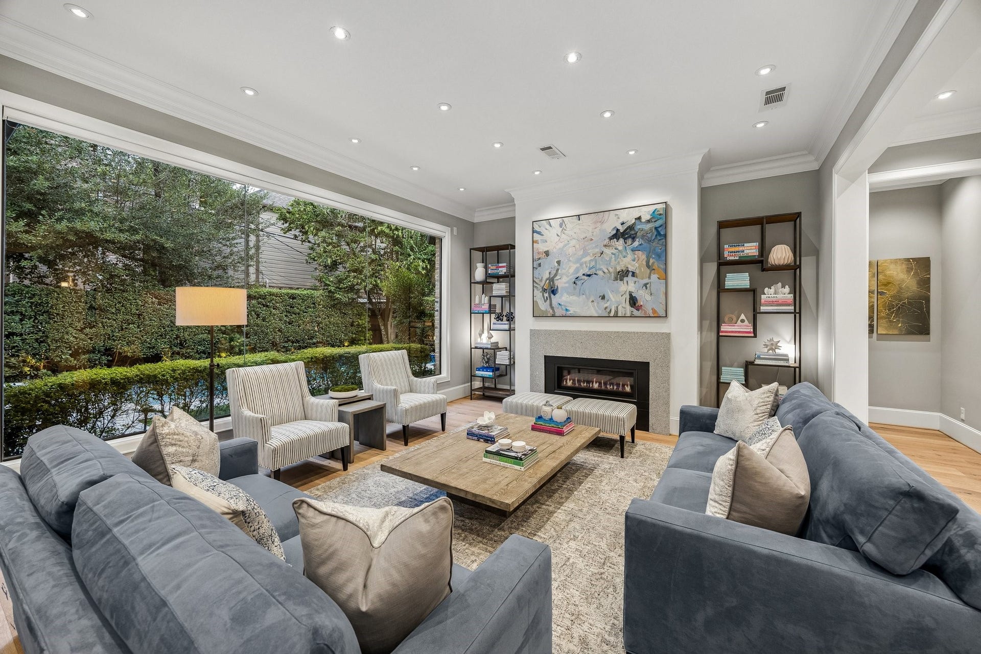 Another view of the living room, which also features, LED recessed lighting, wide plank floors, crown molding and 8 Inch baseboards.  There is also a direct vent, sleek linear fireplace framed by a contemporary stone surround.