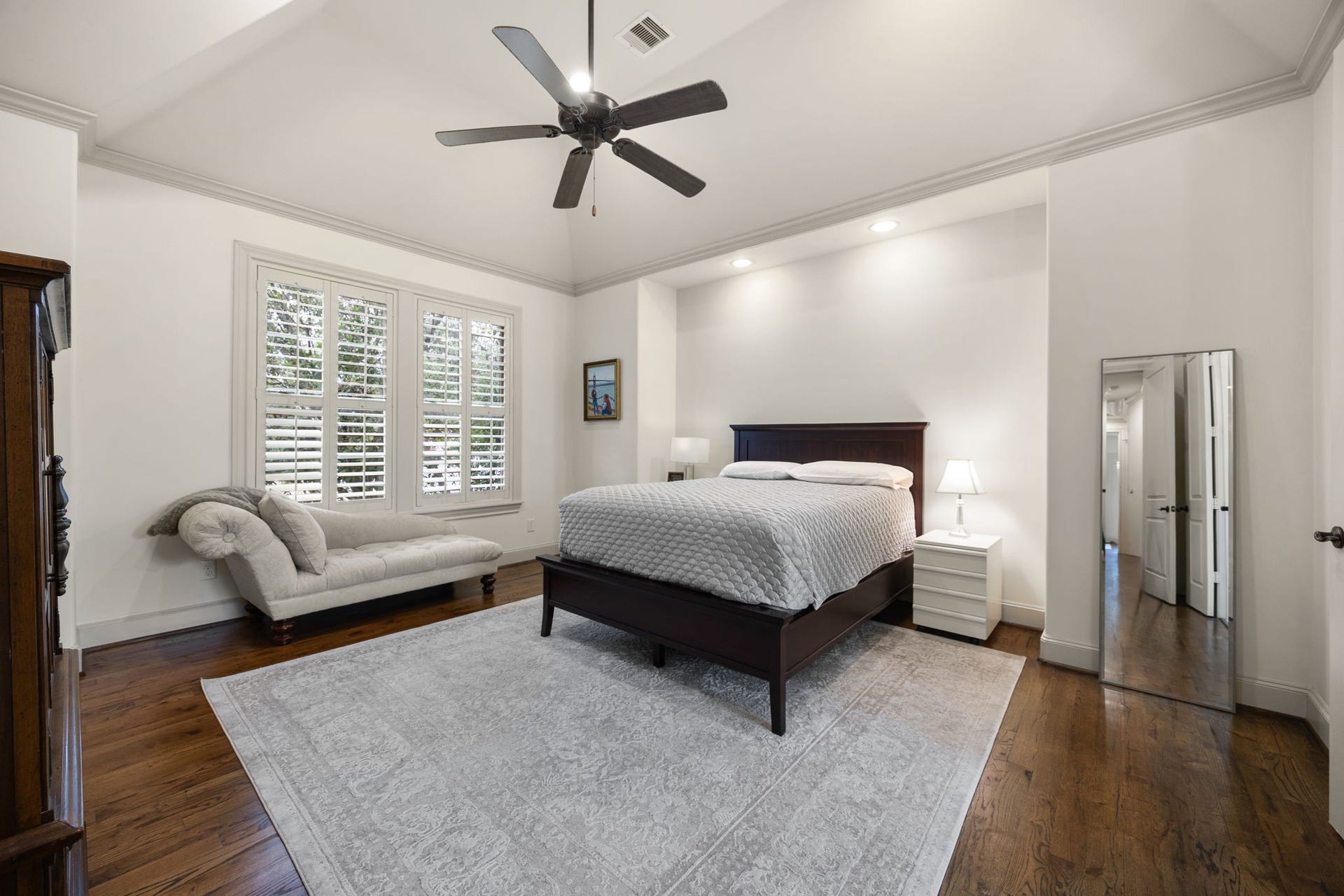 310 W Bell Street, Houston, TX 77019 This spacious primary bedroom features elevated finishes such as a vaulted ceiling, crown moulding, hardwood floors, and shuttered windows. The neutral tones create an elegant place to retreat.