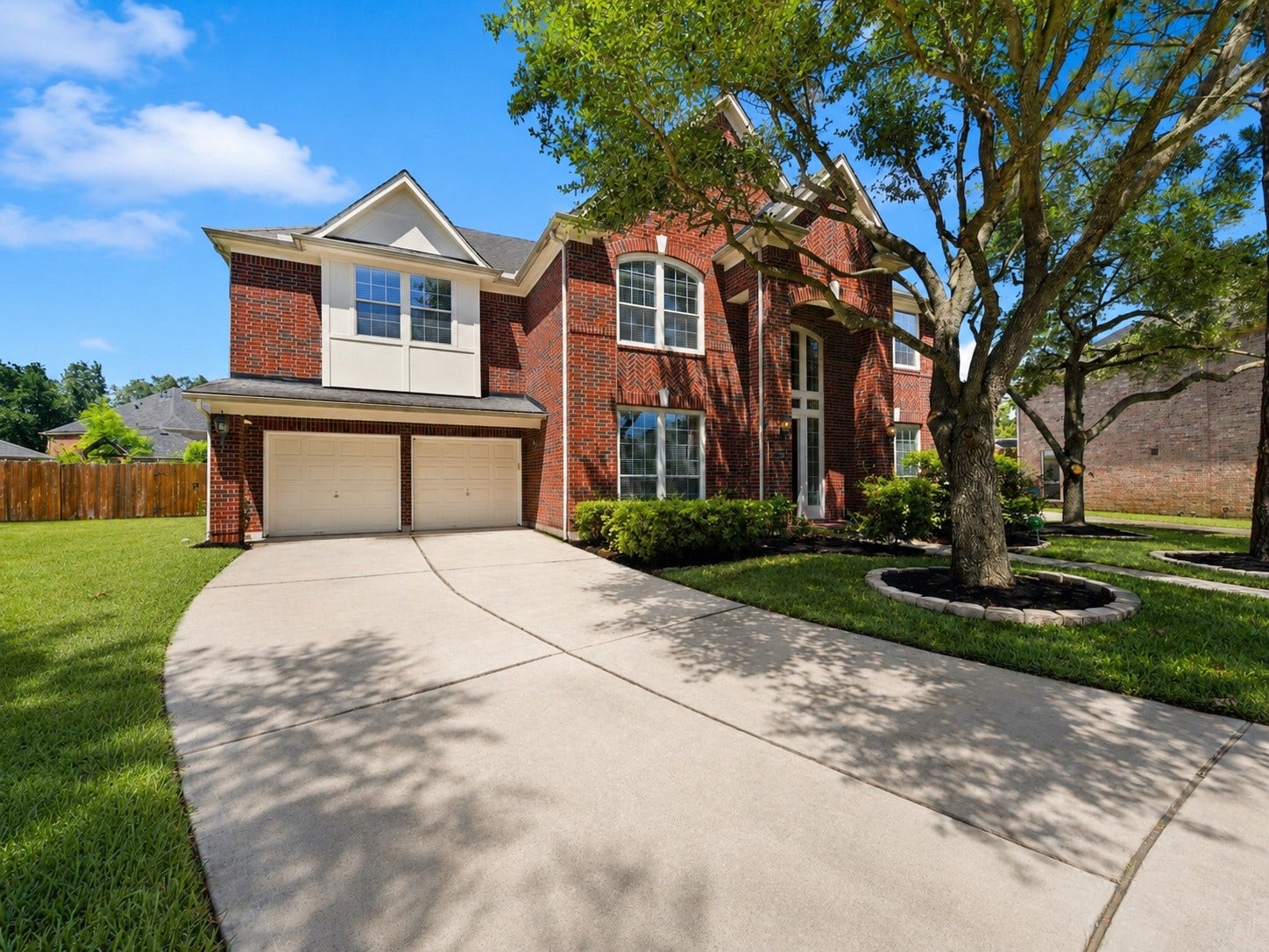 26306 Eden Point Court, Katy, TX 77494 Front elevation with a wide driveway, three-car tandem garage, brick faade, and mature landscaping.