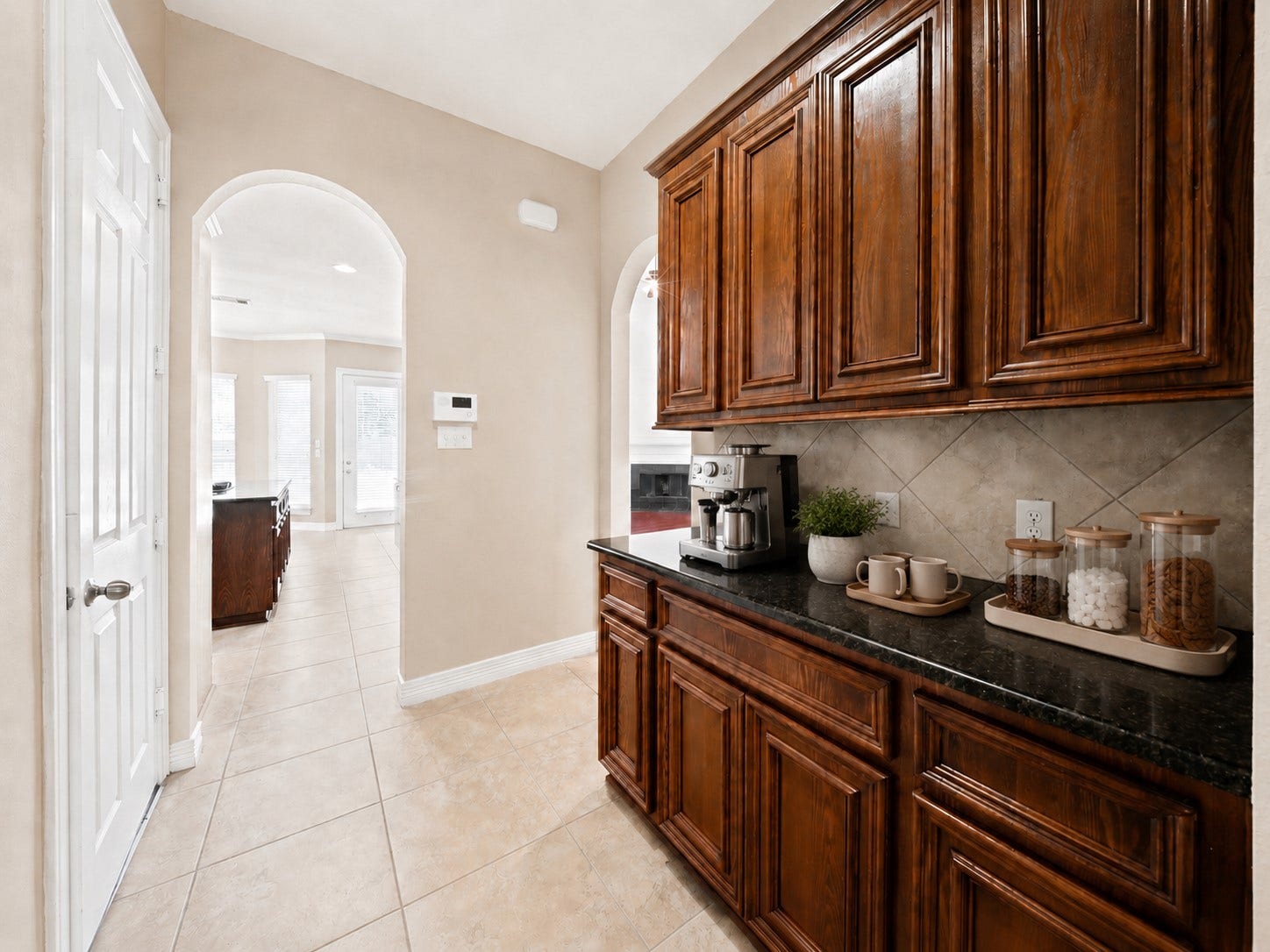 26306 Eden Point Court, Katy, TX 77494 Butlers pantry with rich wood cabinetry, granite countertop, tiled backsplash, and an arched opening toward the dining area.