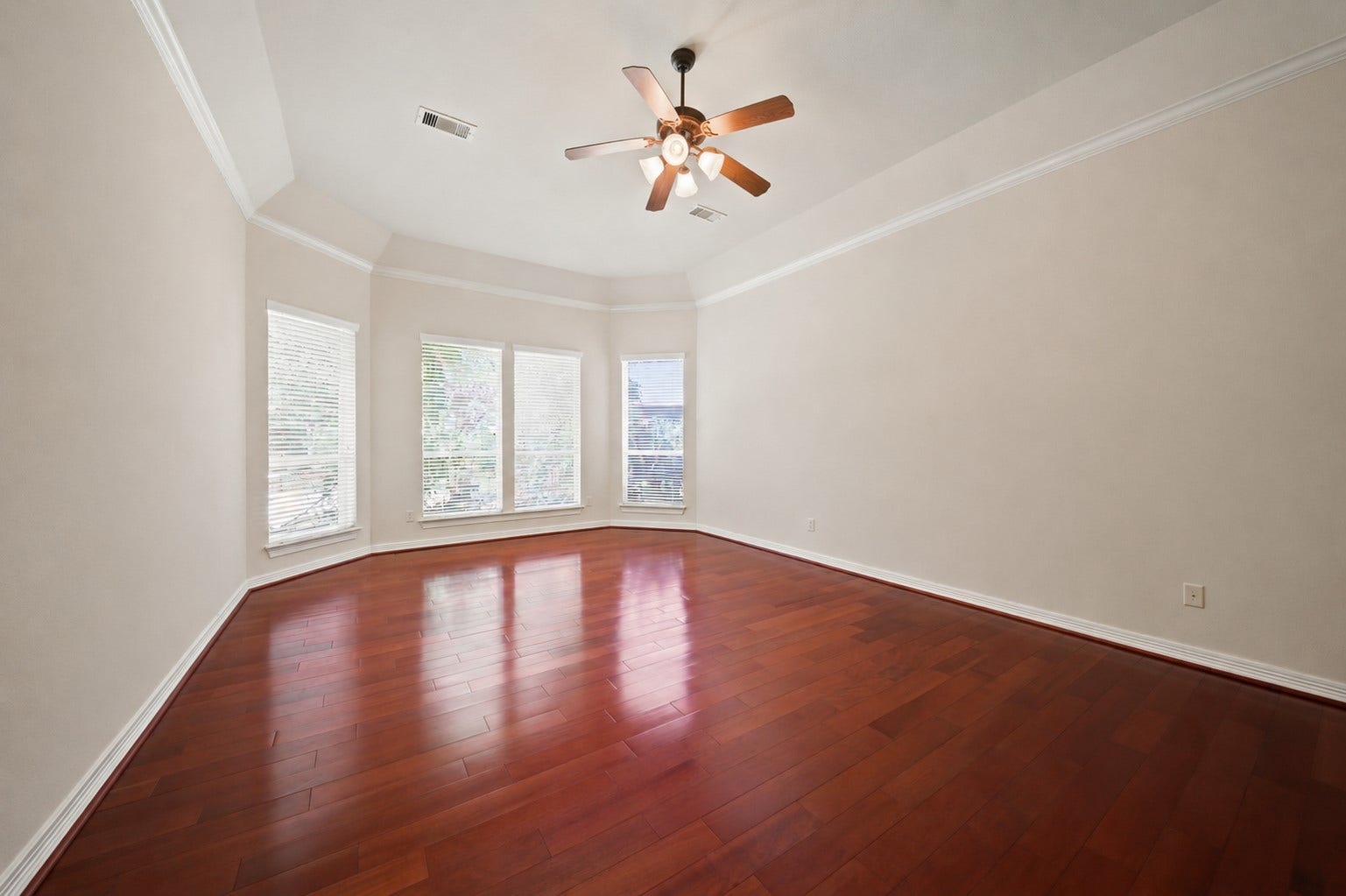 26306 Eden Point Court, Katy, TX 77494 Primary bedroom view highlighting the bay-style window arrangement, tray ceiling, and expansive hardwood flooring.