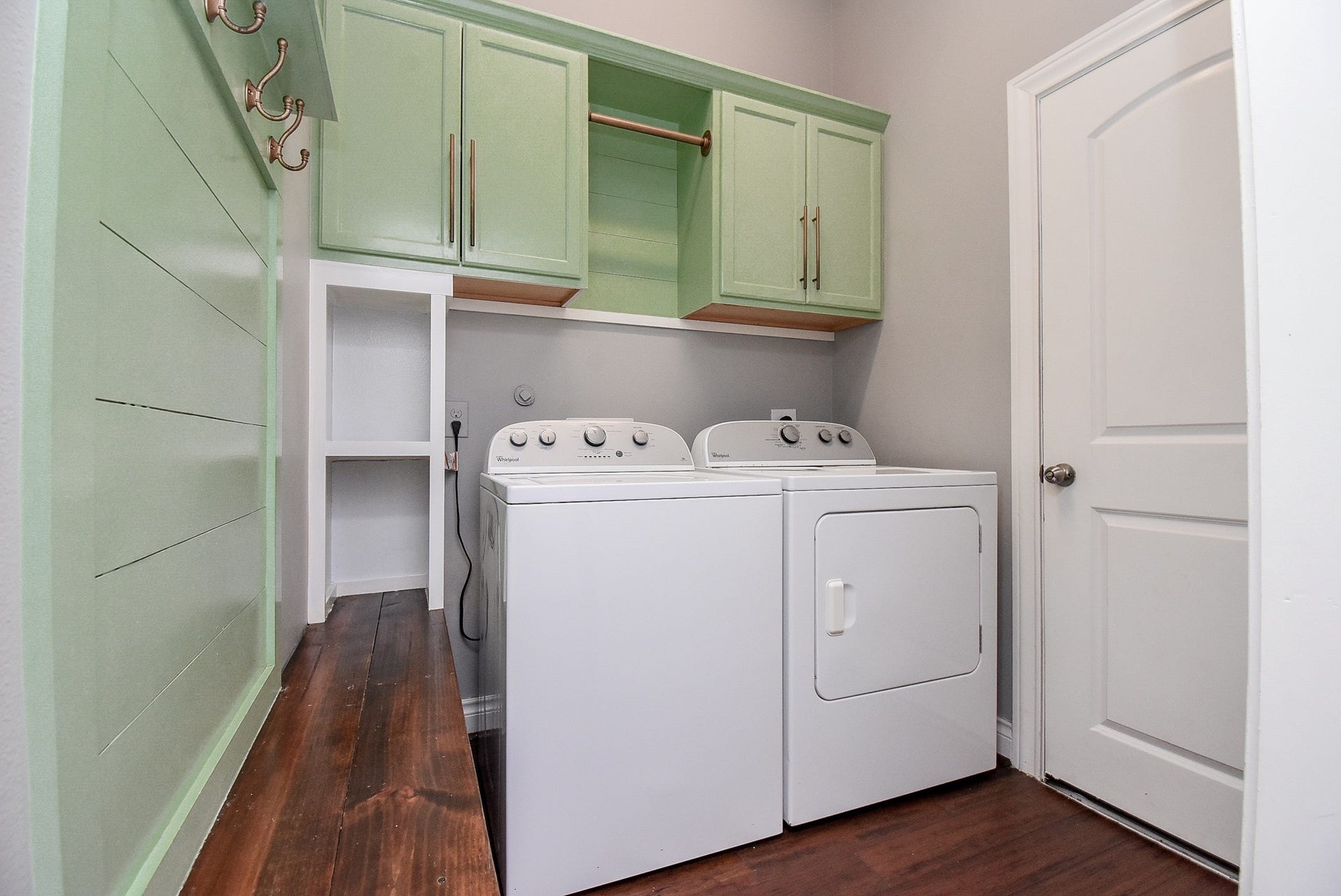 This thoughtfully designed utility room offers everything needed for everyday efficiency, including abundant cabinetry, open shelving, a folding station, wall hooks, and a dedicated hanging area to keep household tasks organized.