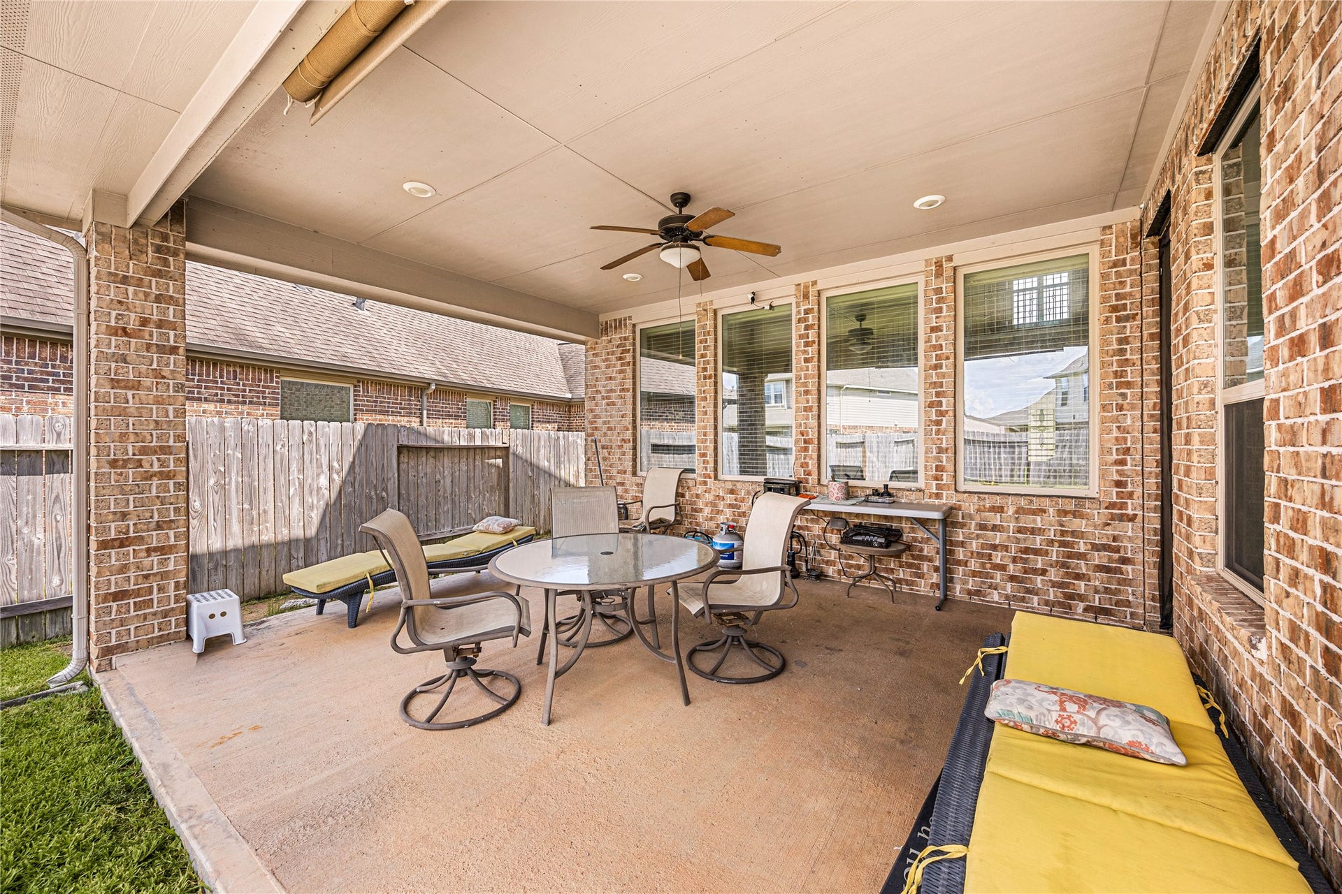 18707 Fox Kestrel Trail, Cypress, TX 77429 Spacious covered patio with ceiling fan, perfect for outdoor entertaining, featuring comfortable seating and a dining set, surrounded by brick accents and a fenced yard for privacy.