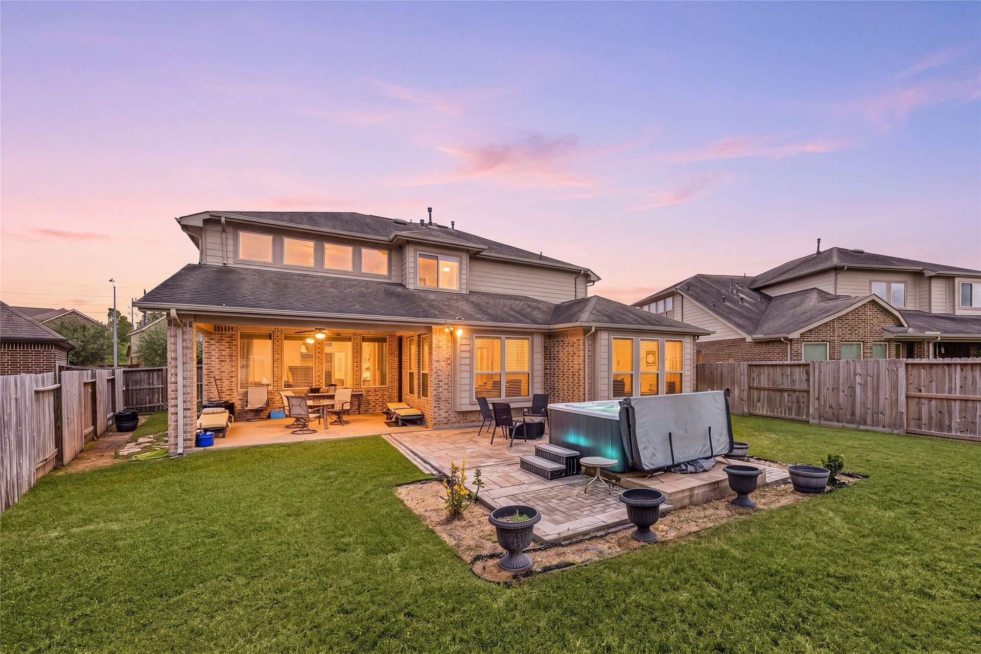 18707 Fox Kestrel Trail, Cypress, TX 77429 Spacious backyard oasis featuring a large patio with a covered seating area, perfect for outdoor entertaining, and a hot tub for relaxation, all set against a beautiful sunset backdrop.