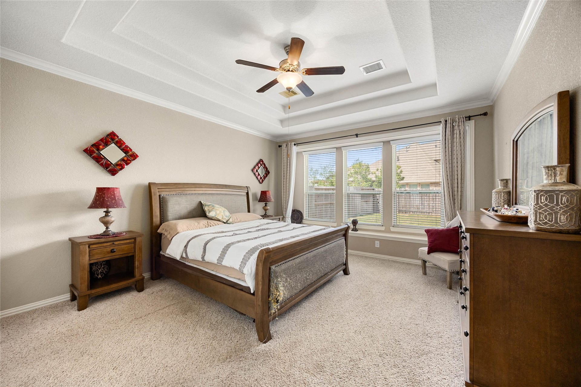 18707 Fox Kestrel Trail, Cypress, TX 77429 Spacious bedroom featuring a tray ceiling, elegant ceiling fan, and abundant natural light from large windows overlooking the backyard.