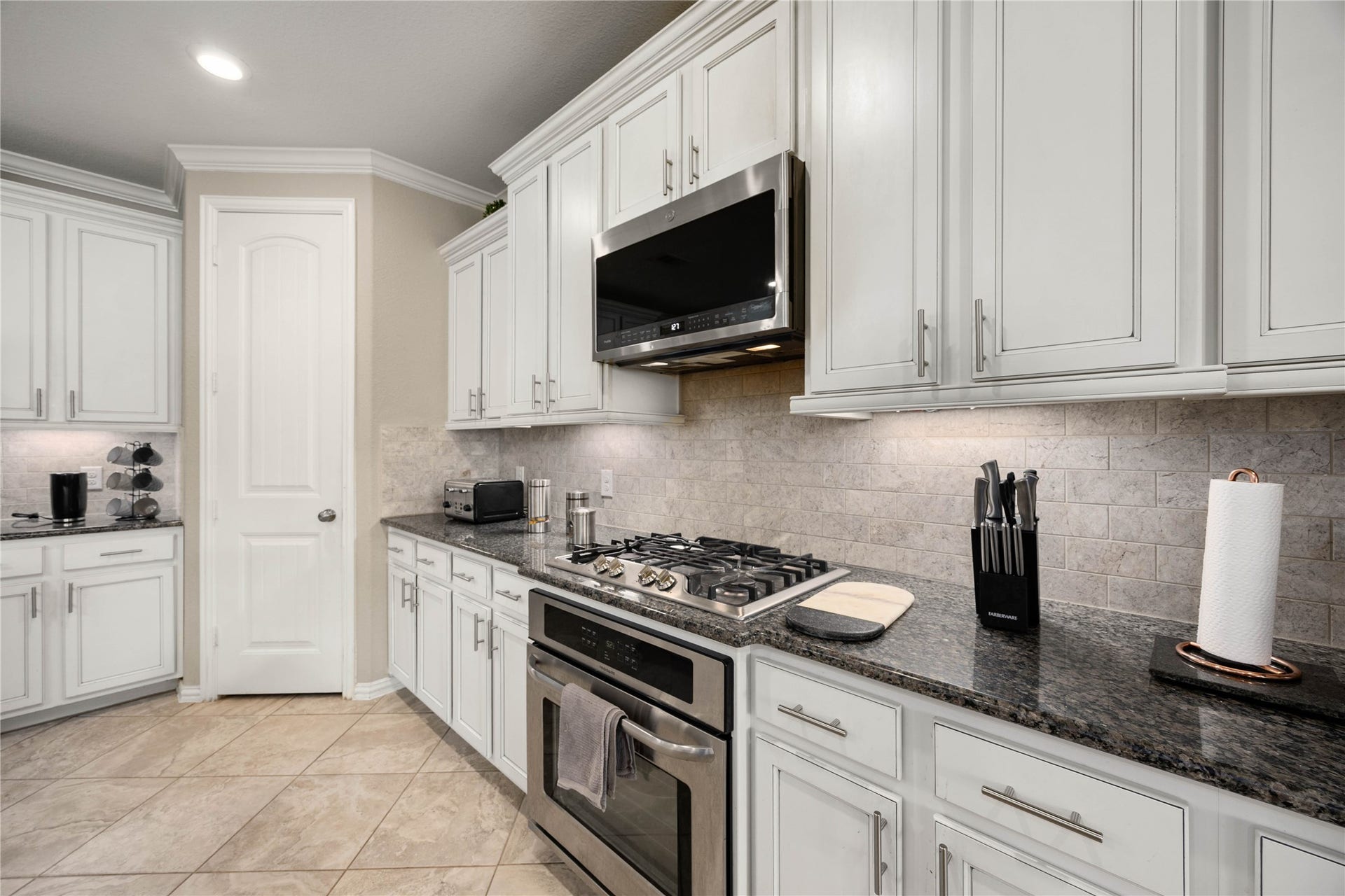 18707 Fox Kestrel Trail, Cypress, TX 77429 Sleek kitchen with modern stainless steel appliances, elegant white cabinetry, and granite countertops, enhanced by a stylish subway tile backsplash.