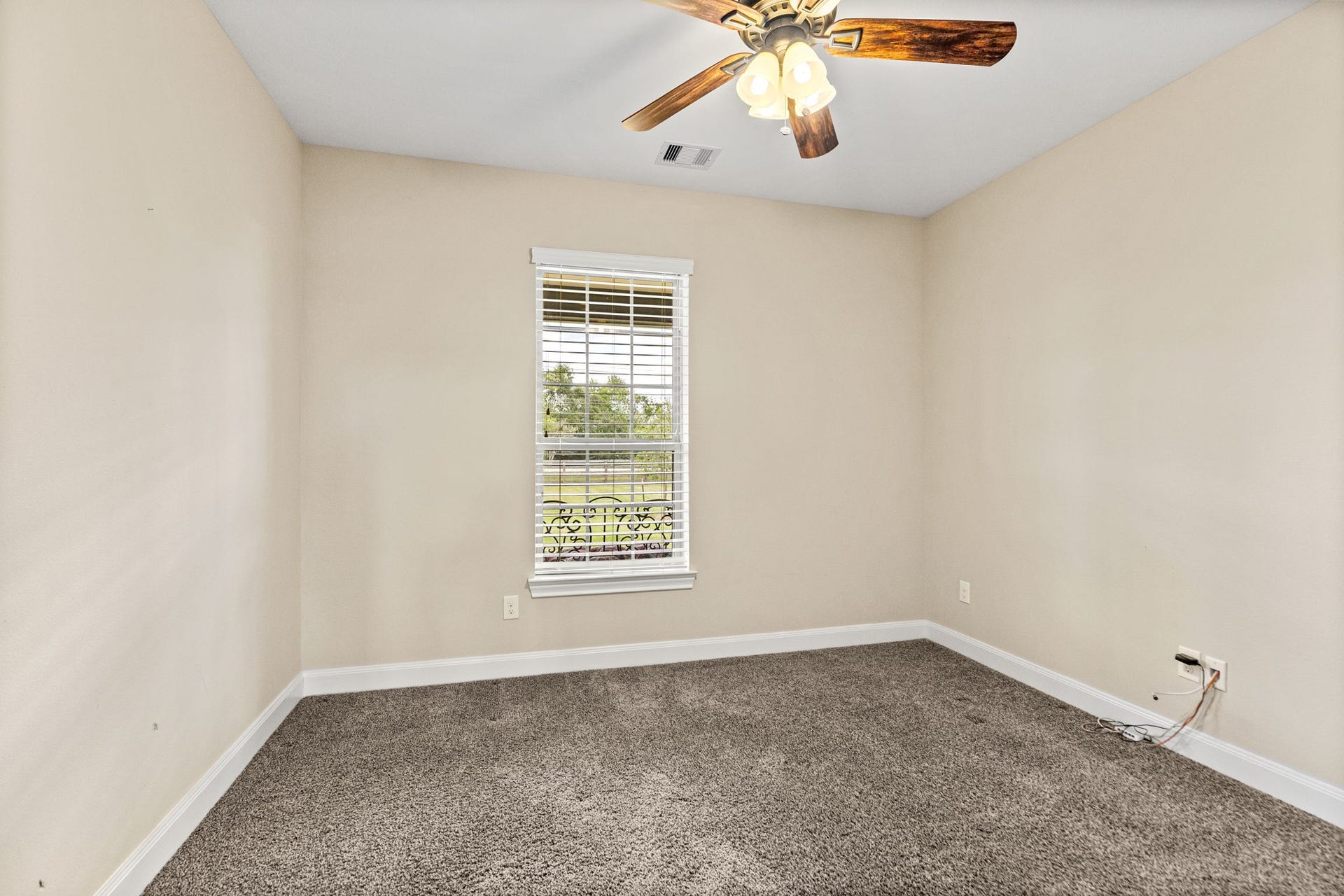 Cozy room with soft carpet flooring, a ceiling fan with lights, and a window offering a pleasant outdoor view.