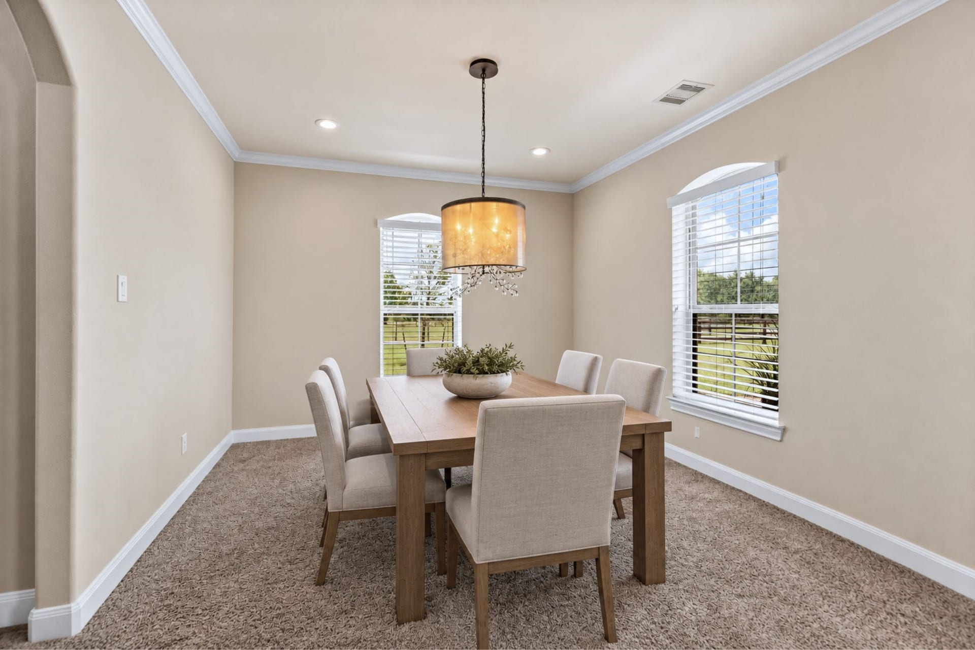 Elegant dining room with soft beige walls, plush carpeting, and a modern chandelier, offering a cozy and inviting atmosphere.