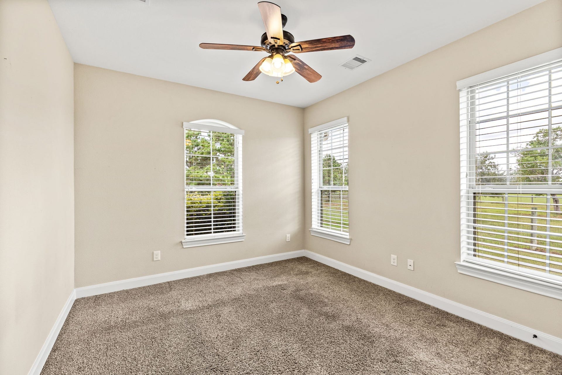 Bright and inviting bedroom featuring large windows with serene views, plush carpeting, and a stylish ceiling fan.