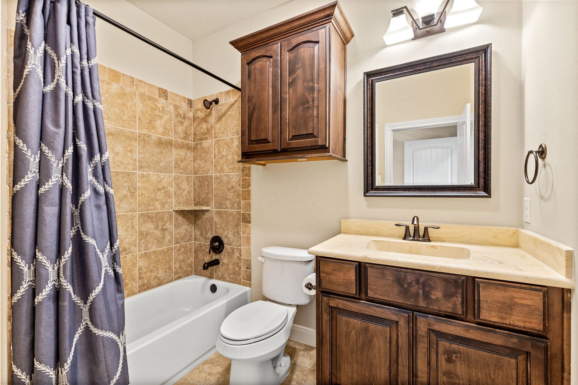 Charming bathroom featuring a tiled shower and tub combo, elegant wood cabinetry, and a stylish vanity with a matching framed mirror.