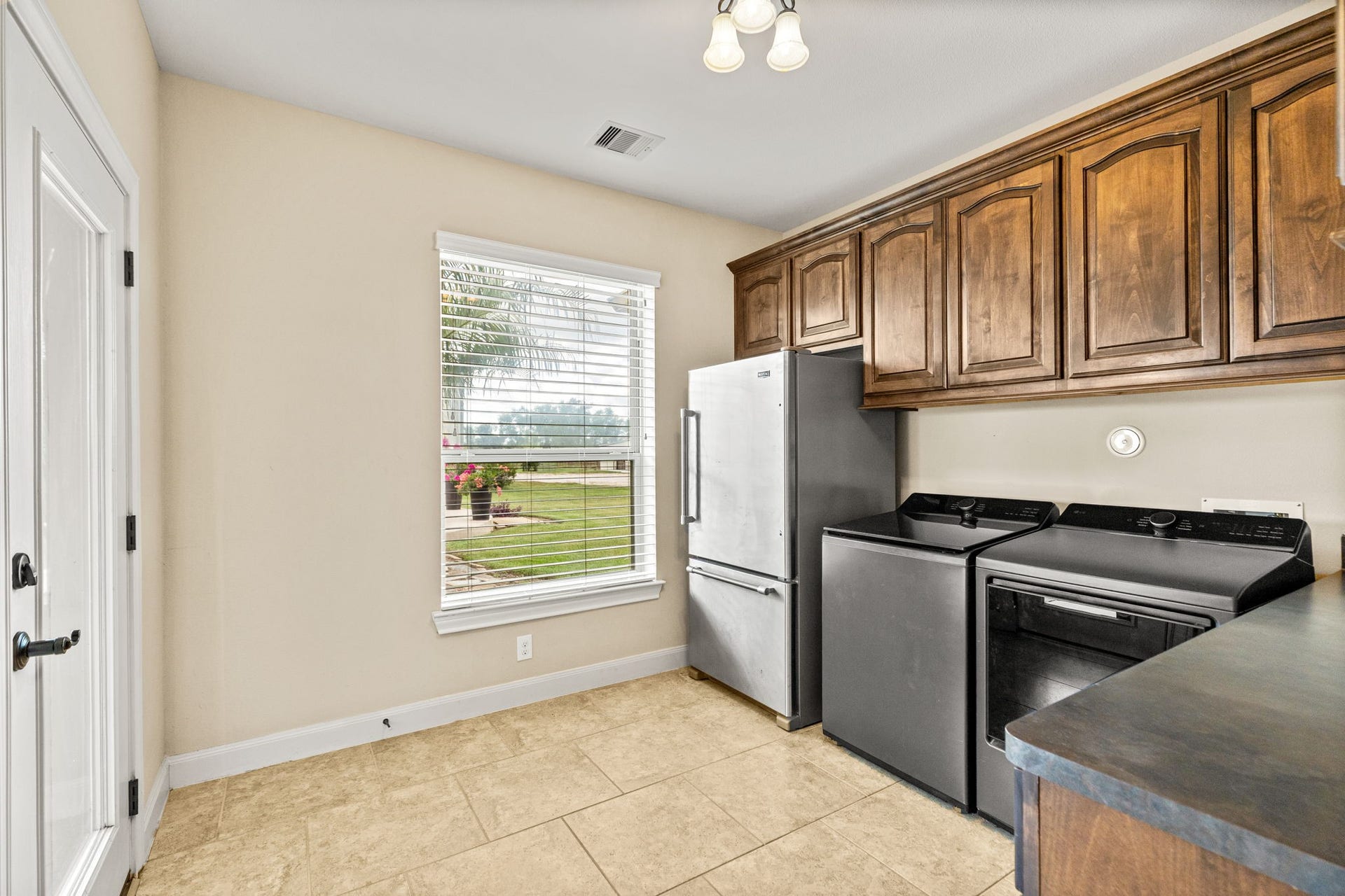 Bright and functional utility room featuring modern appliances, ample wooden cabinetry, and a view of the landscaped yard.