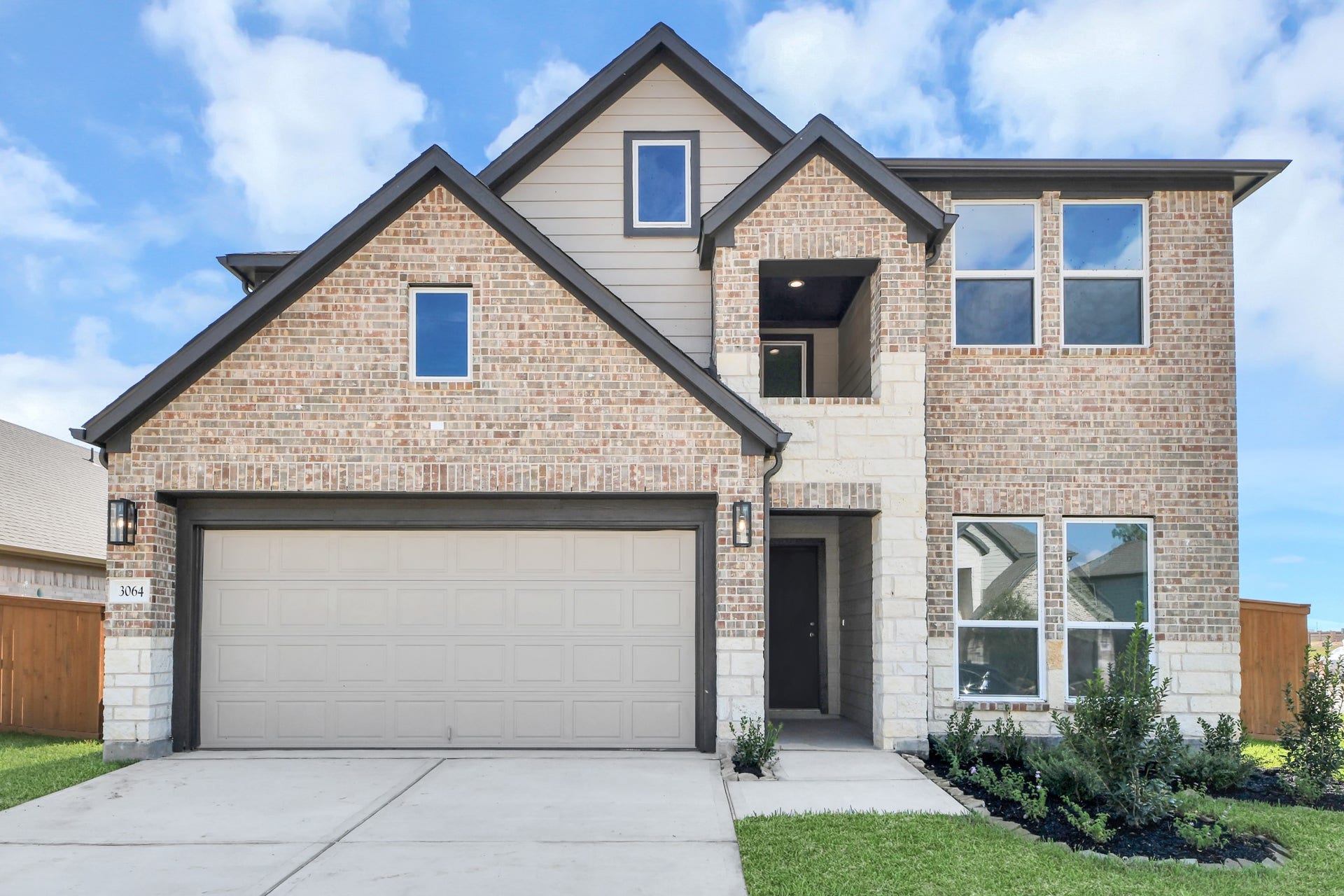 3064 Spoolwood Trail, Magnolia, TX 77355 This home boasts lush green grass and meticulous landscaping. Its premium elevation showcases an exquisite blend of brick and stone features, complemented by modern coach lighting