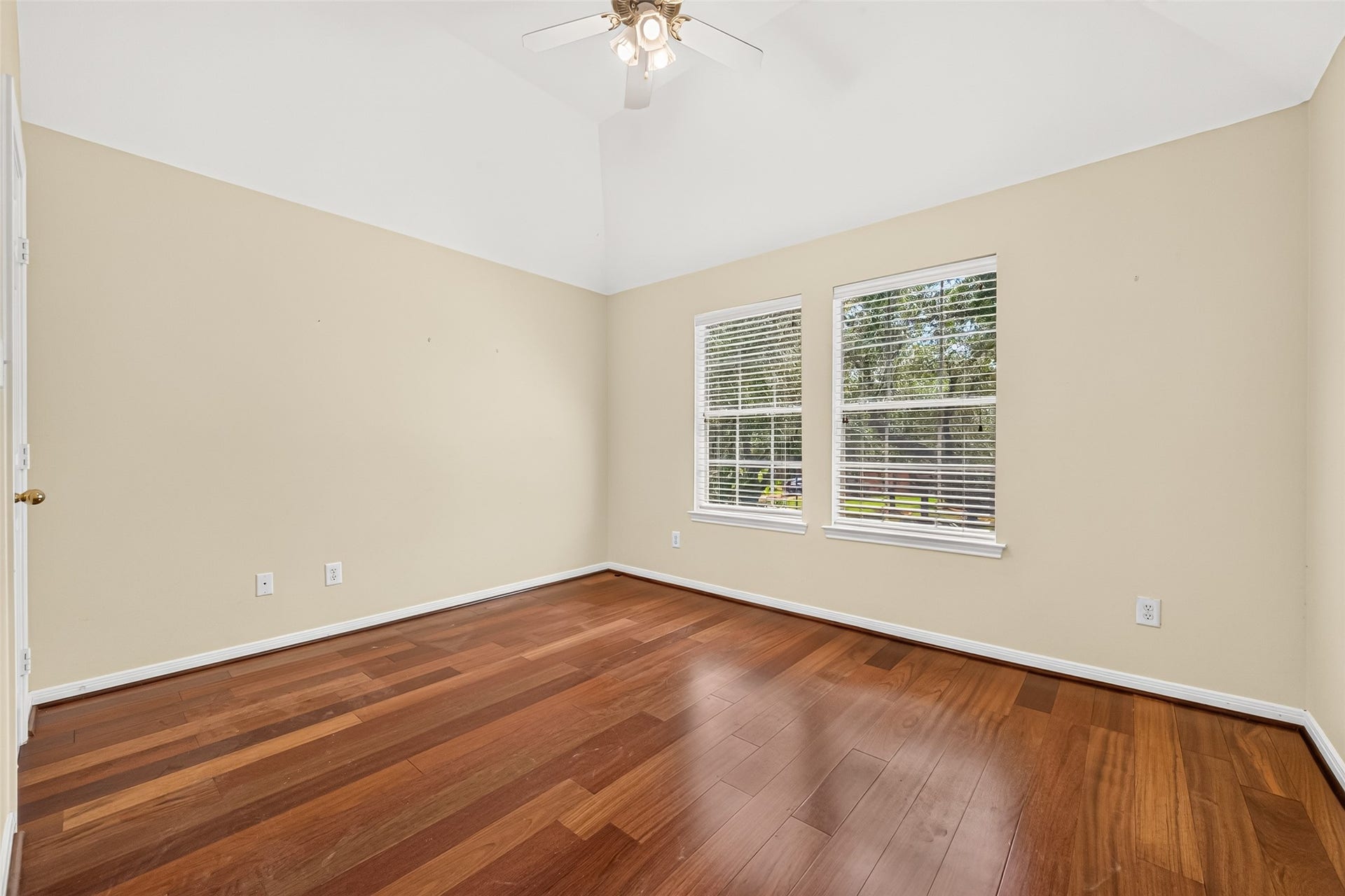 1711 Emma Cove Court, Sugar Land, TX 77479 Neutral-toned bedroom offers hardwood floors, a ceiling fan, and a pair of windows overlooking mature trees.