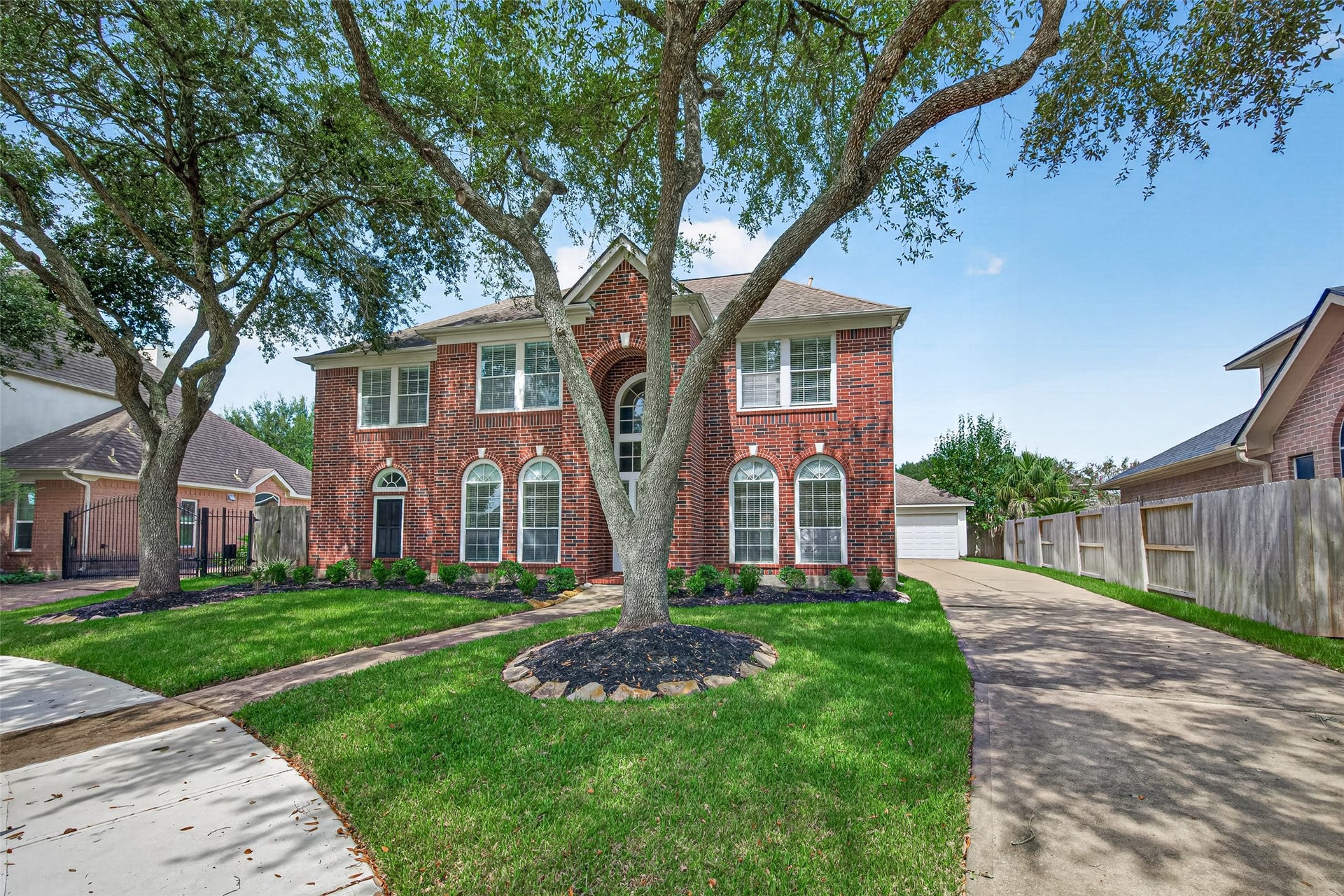 1711 Emma Cove Court, Sugar Land, TX 77479 Stately two-story brick home showcases mature shade trees, manicured landscaping, arched windows, and a long driveway leading to the detached garage.