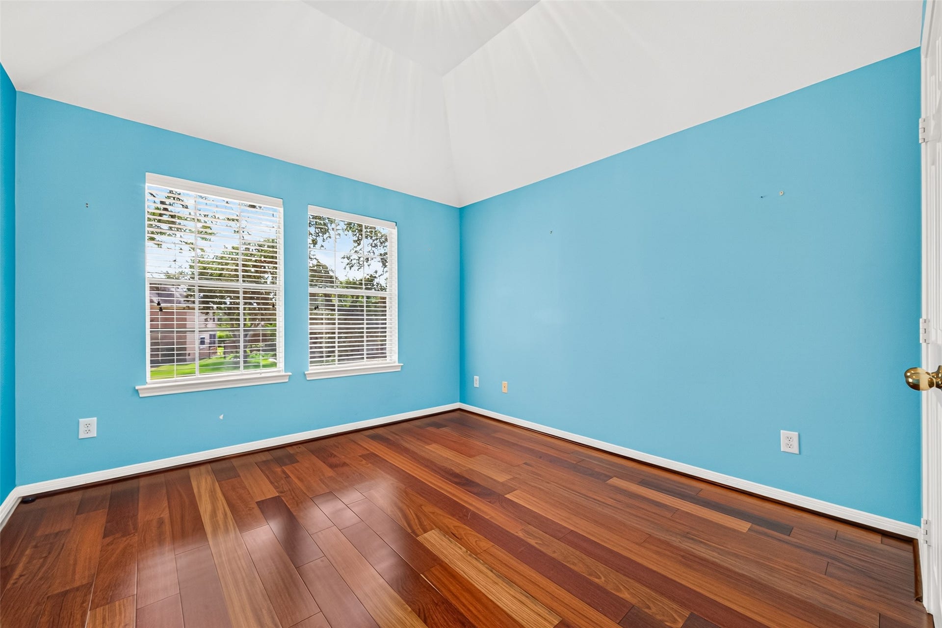 1711 Emma Cove Court, Sugar Land, TX 77479 Vibrant secondary bedroom pairs rich wood flooring with a vaulted ceiling and two sunlit windows.