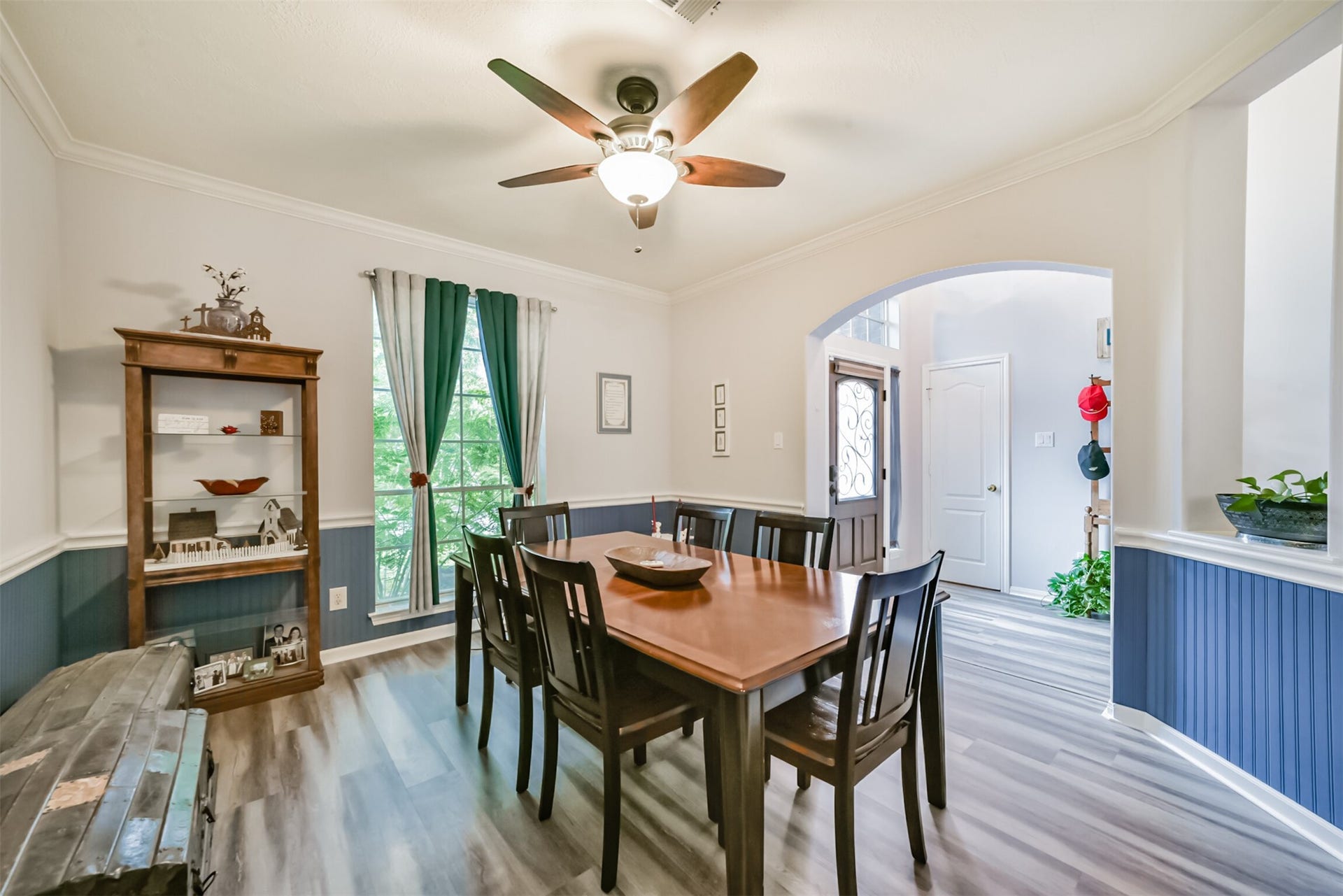 18402 Spinner Court Drive, Humble, TX 77346 This formal dining room is defined by elegant crown and chair molding, with Beadboard accenting the walls. A ceiling fan with an integrated light fixture hangs overhead, while curtains frame the large window.